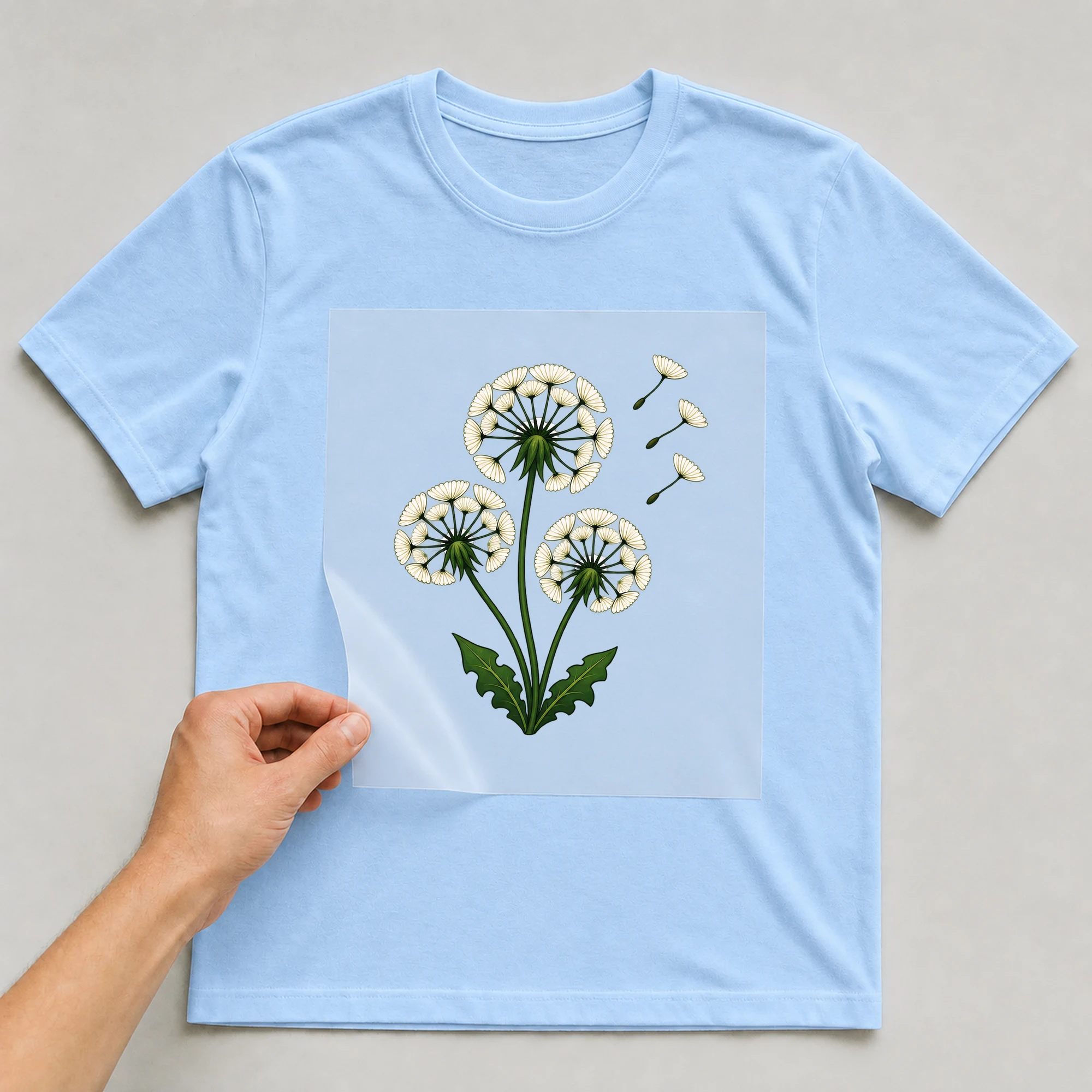Bügelbild „Pusteblumen“ auf babyblauem T-Shirt, Folie wird aufgelegt