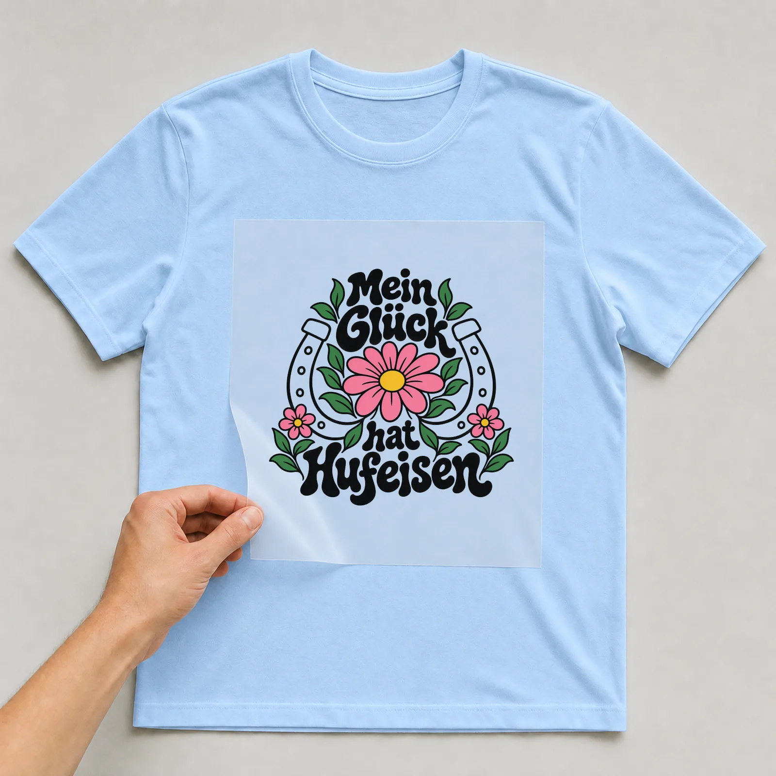 Bügelbild „Mein Glück hat Hufeisen“ auf hellblauem T-Shirt, Folie wird aufgelegt