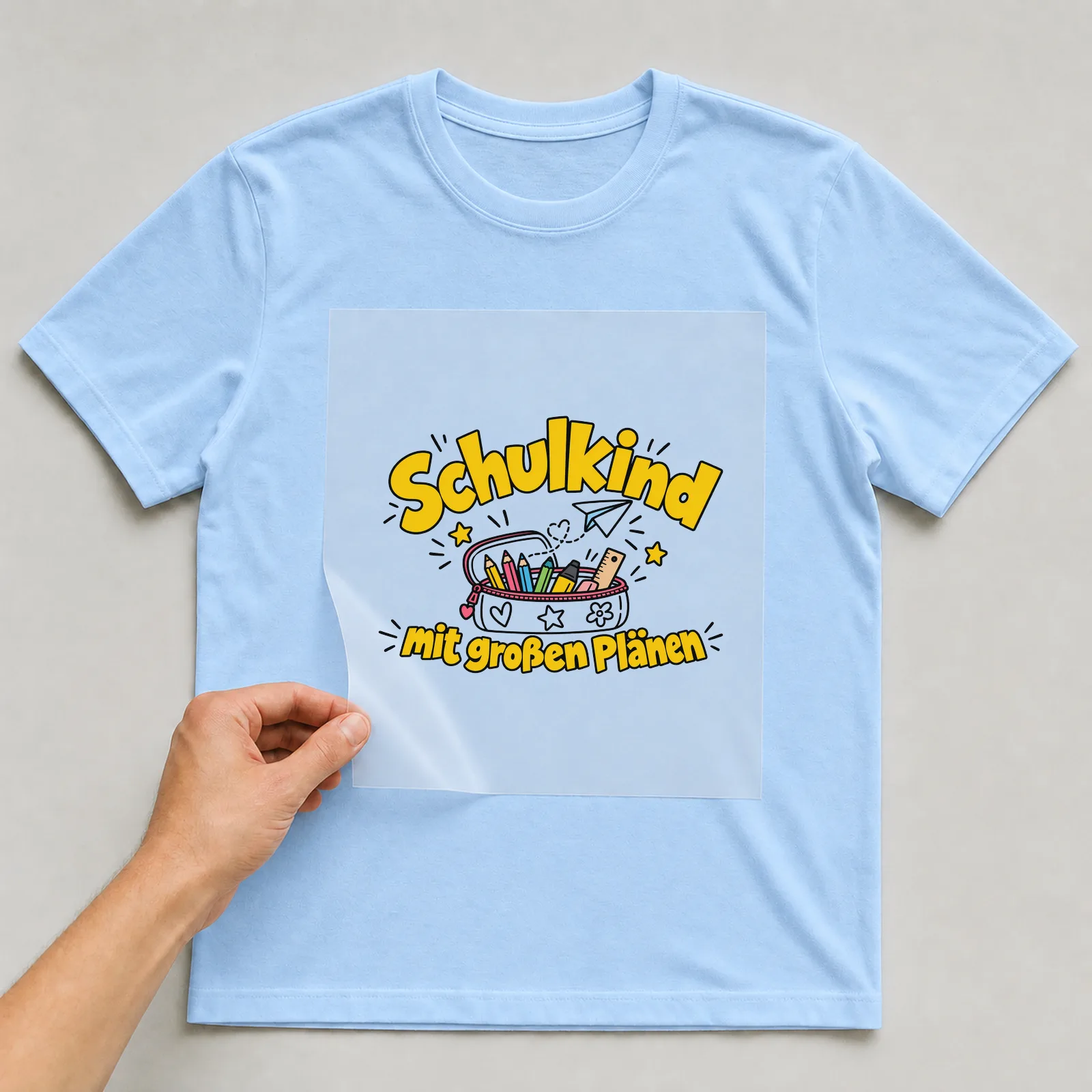 Bügelbild „Schulkind mit großen Plänen“ auf hellblauem T-Shirt, Folie wird aufgelegt