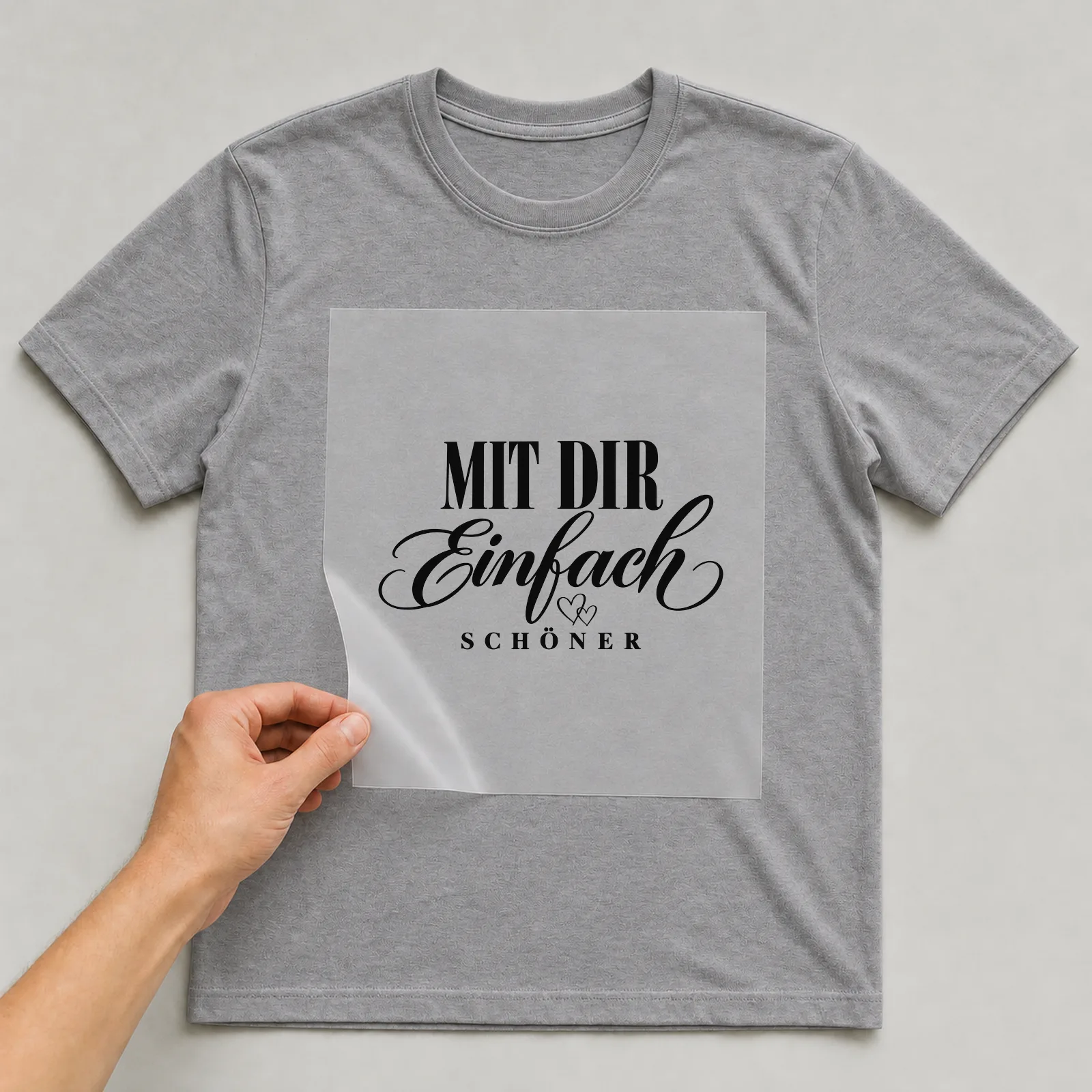Bügelbild „Mit dir einfach schöner“ auf grauem T-Shirt, Folie wird aufgelegt