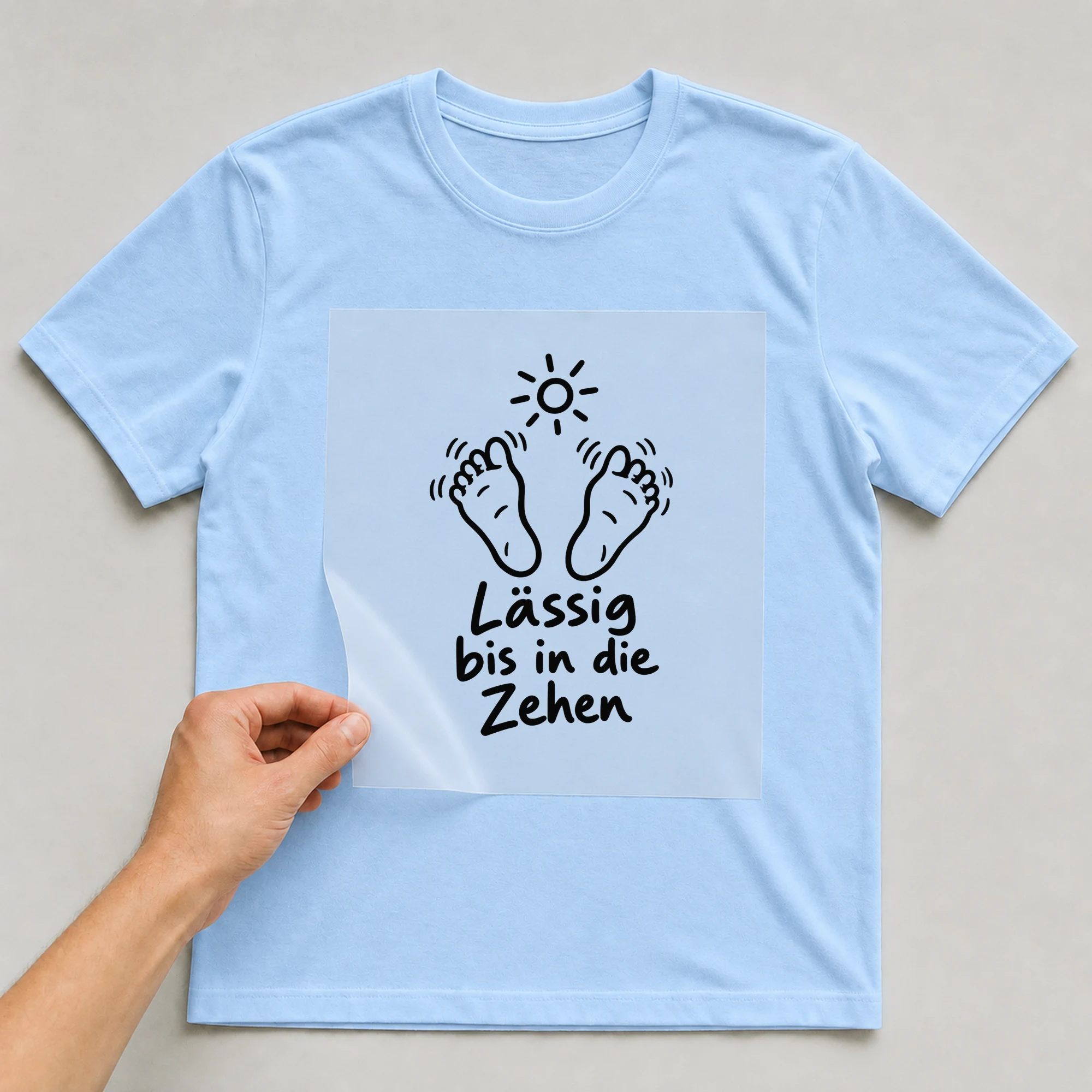 Bügelbild „Lässig bis in die Zehen“ auf babyblauem T-Shirt, Folie wird aufgelegt