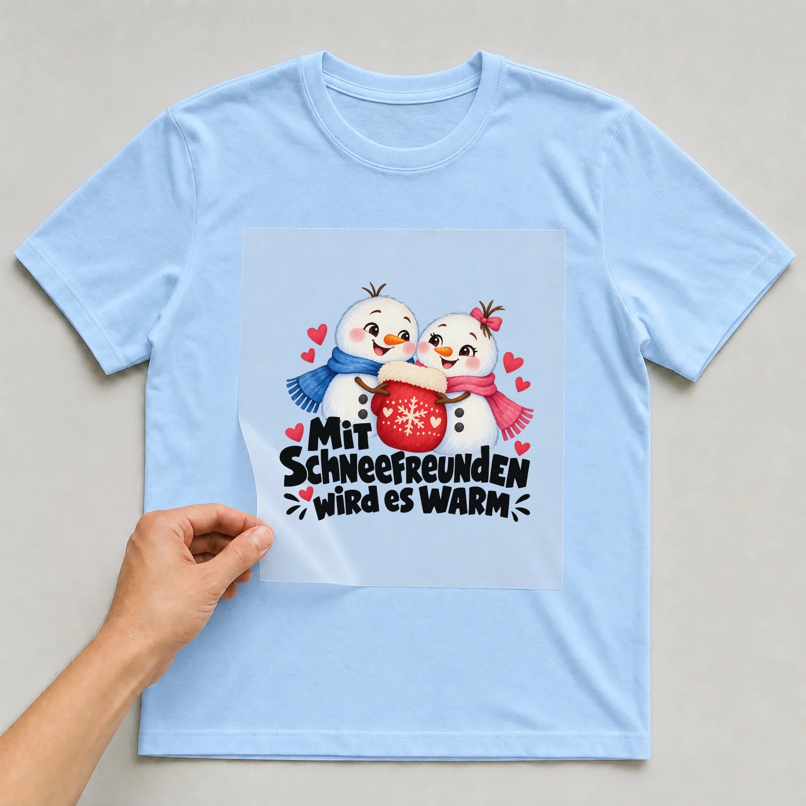 Bügelbild „Mit SCHNEEFREUNDEN wird es WARM“ auf hellblauem T-Shirt, Folie wird aufgelegt