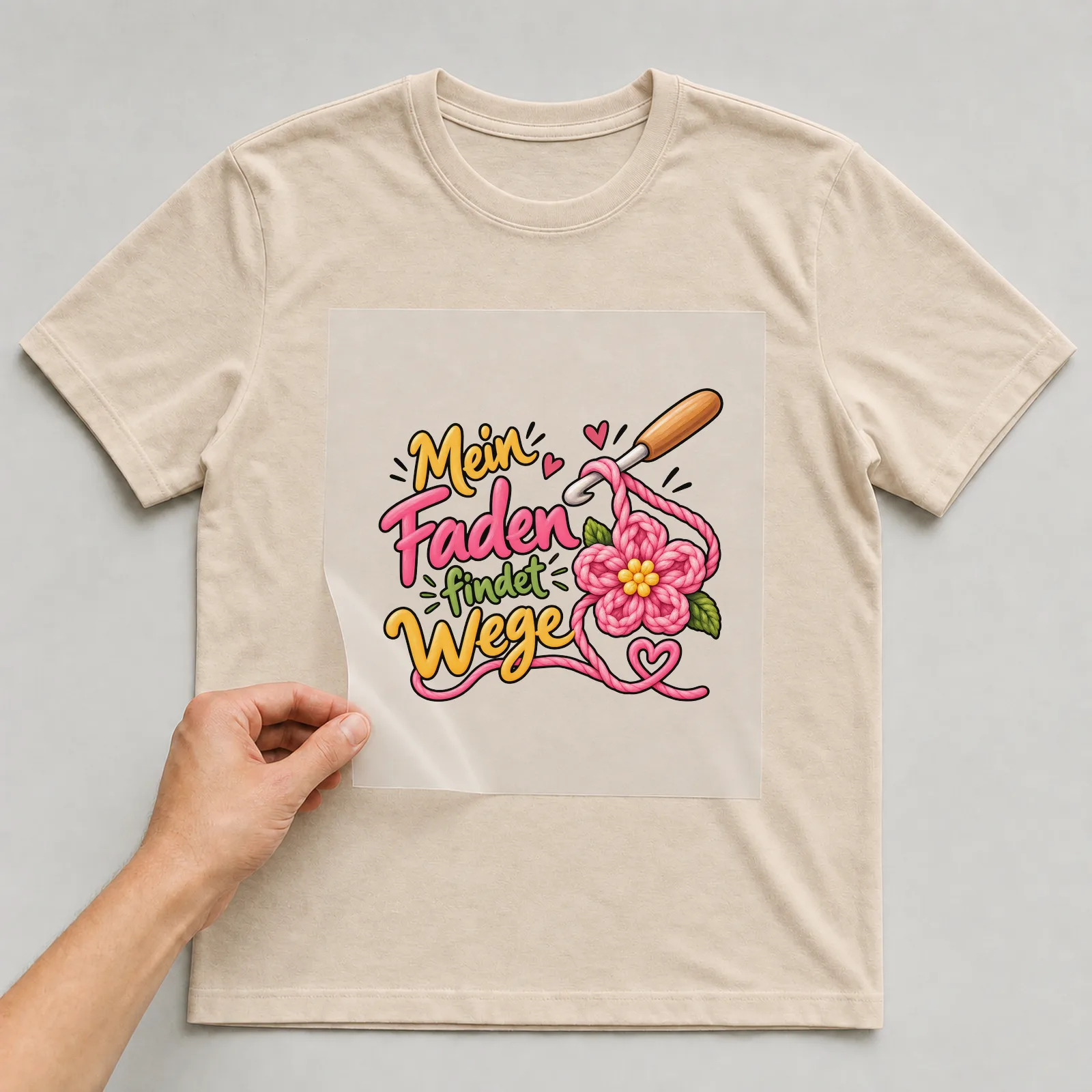 Bügelbild „Mein Faden findet Wege“ auf beigem T-Shirt, Folie wird aufgelegt