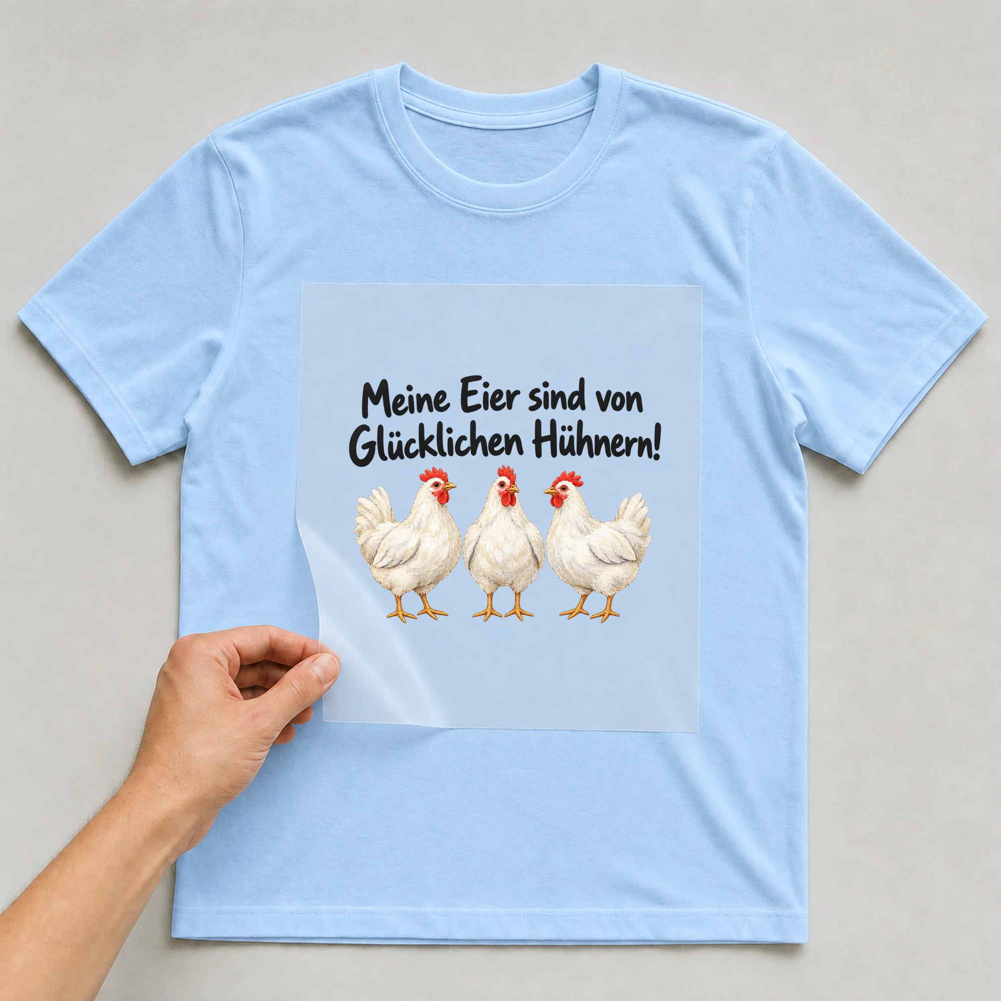 Bügelbild „Meine Eier sind von Glücklichen Hühnern!“ auf babyblauem T-Shirt, Folie wird aufgelegt