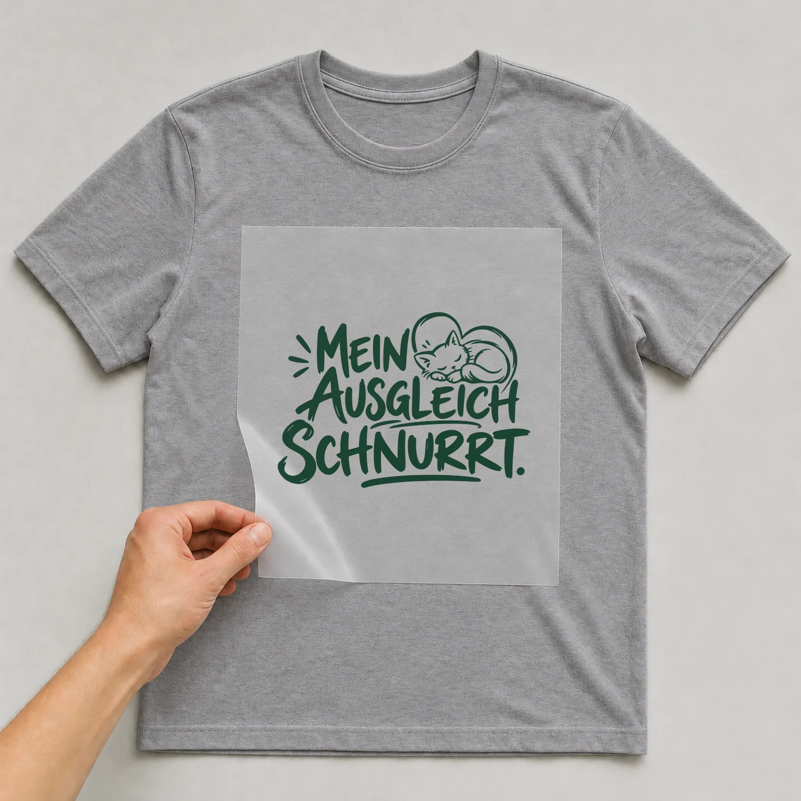 Bügelbild „Mein Ausgleich schnurrt“ auf grauem T-Shirt, Folie wird aufgelegt