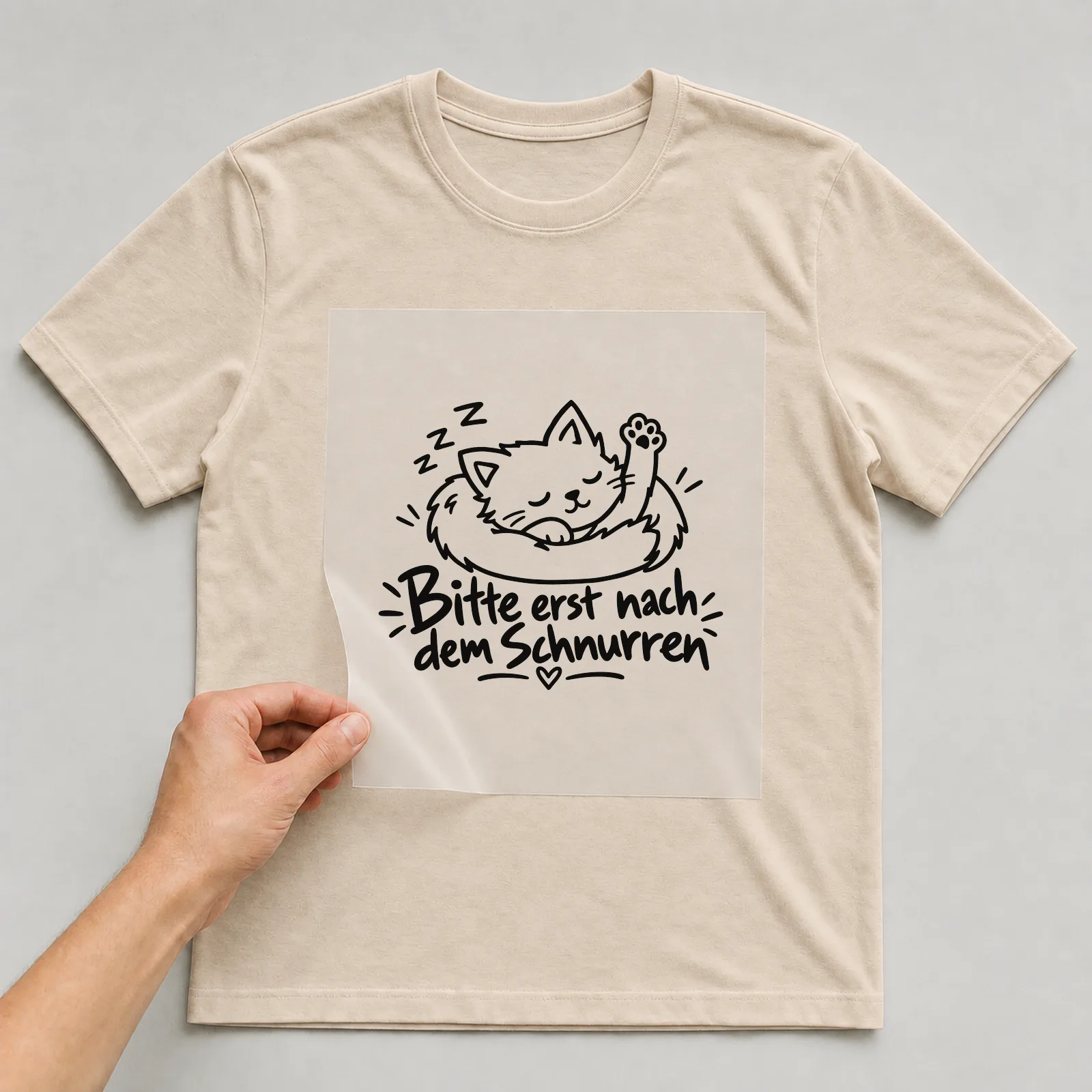Bügelbild „Bitte erst nach dem Schnurren“ auf beigem T-Shirt, Folie wird aufgelegt