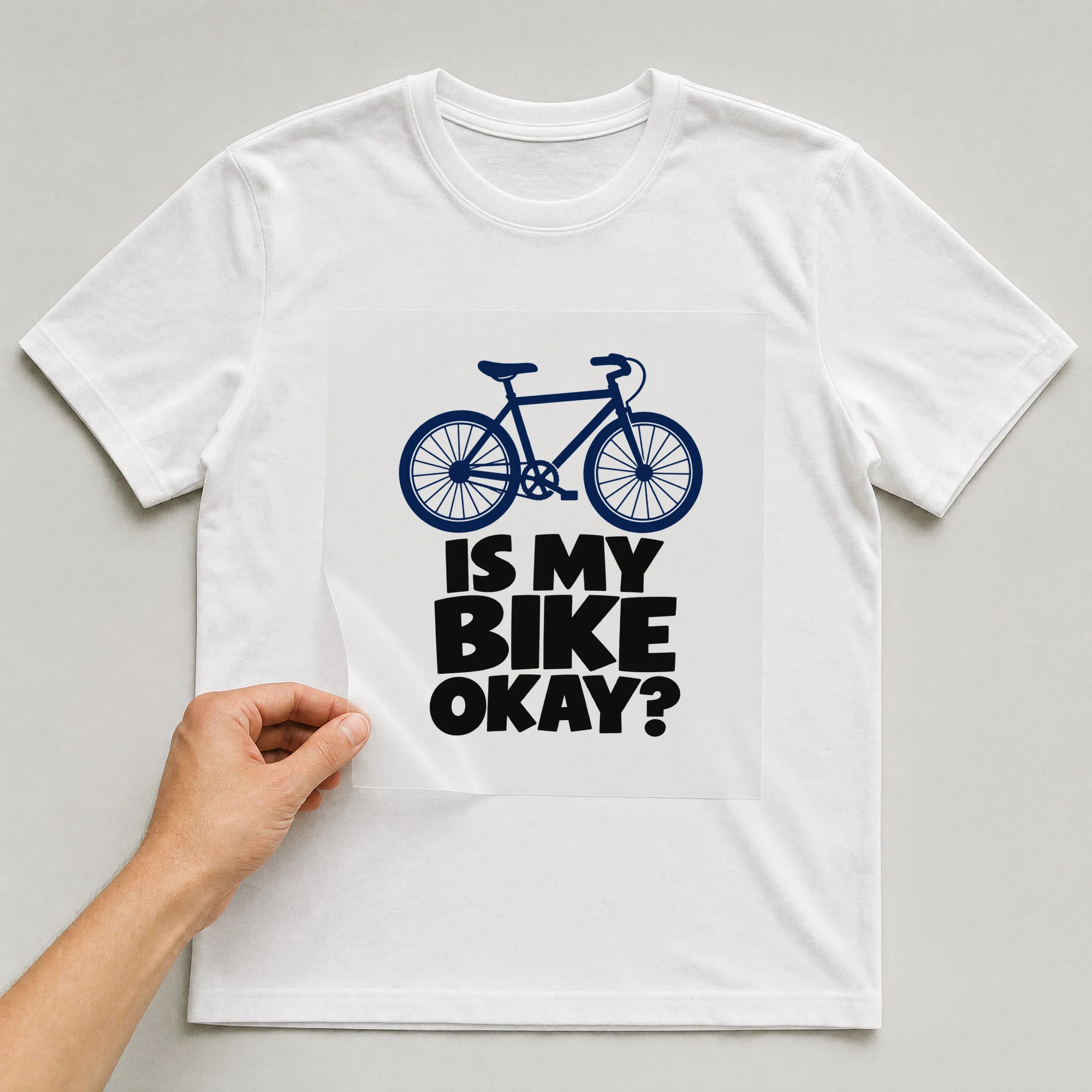 Bügelbild „Is My Bike Okay?“ auf weißem T-Shirt, Folie wird aufgelegt