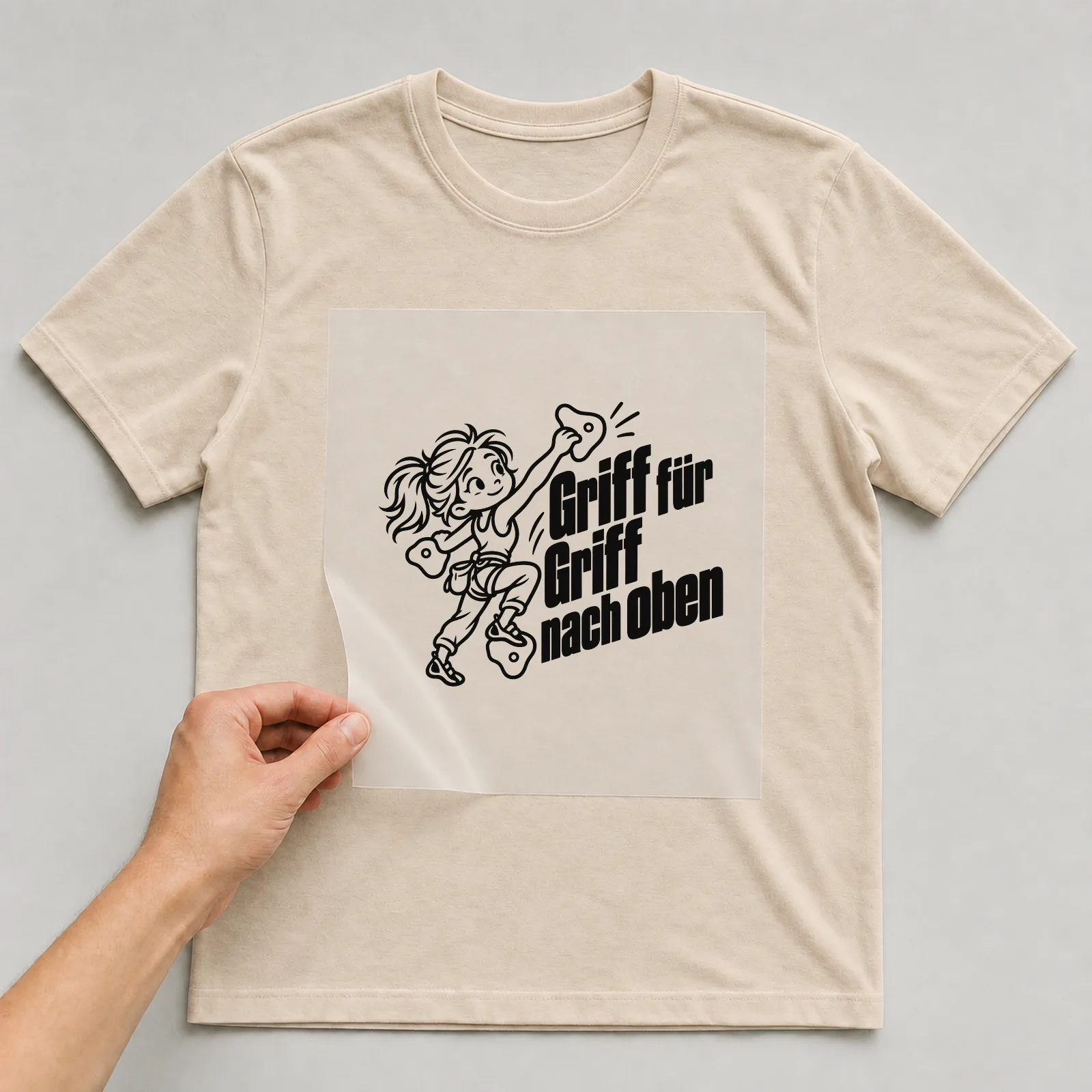 Bügelbild „Griff für Griff nach oben“ auf beigem T-Shirt, Folie wird aufgelegt