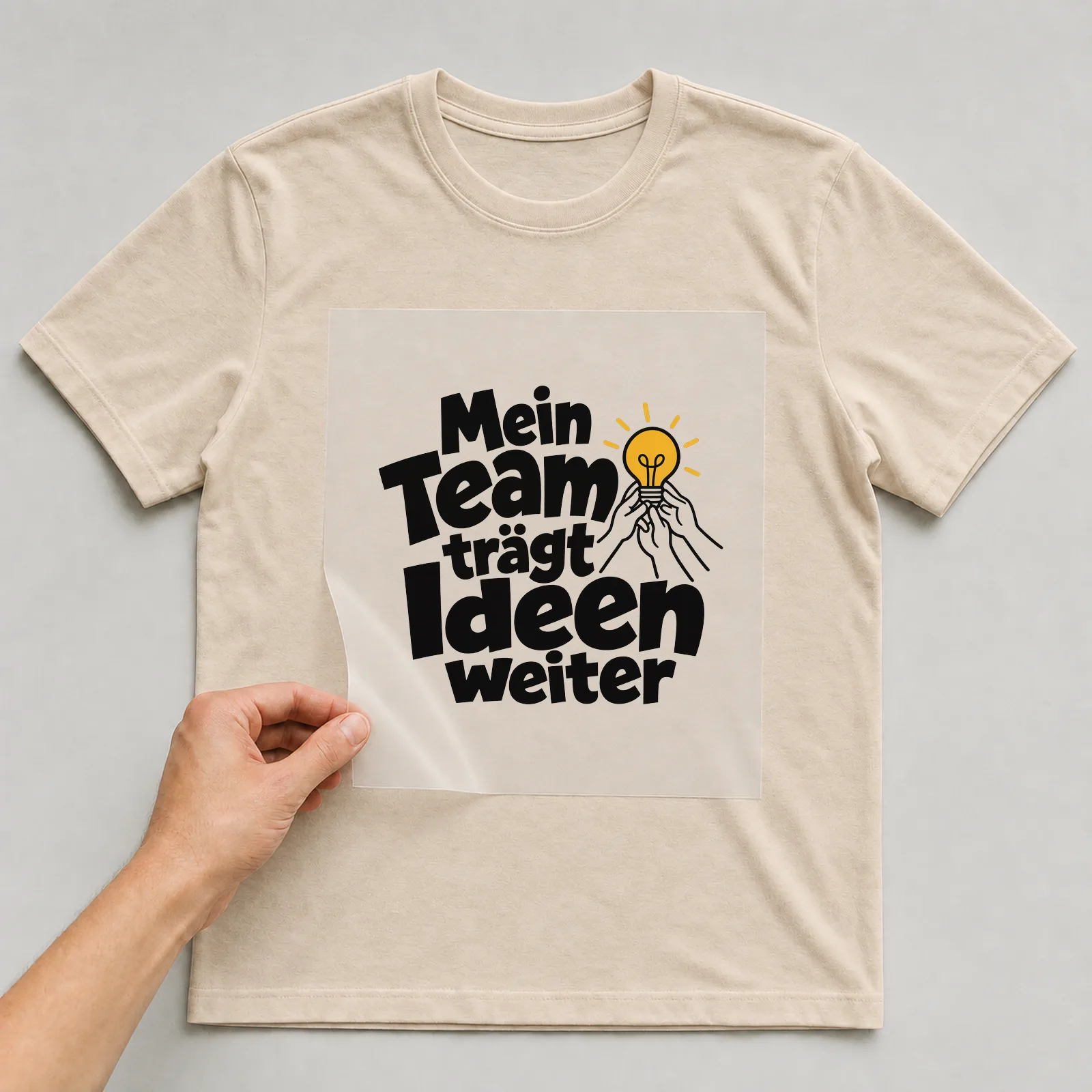 Bügelbild „Mein Team trägt Ideen weiter“ auf beigem T-Shirt, Folie wird aufgelegt
