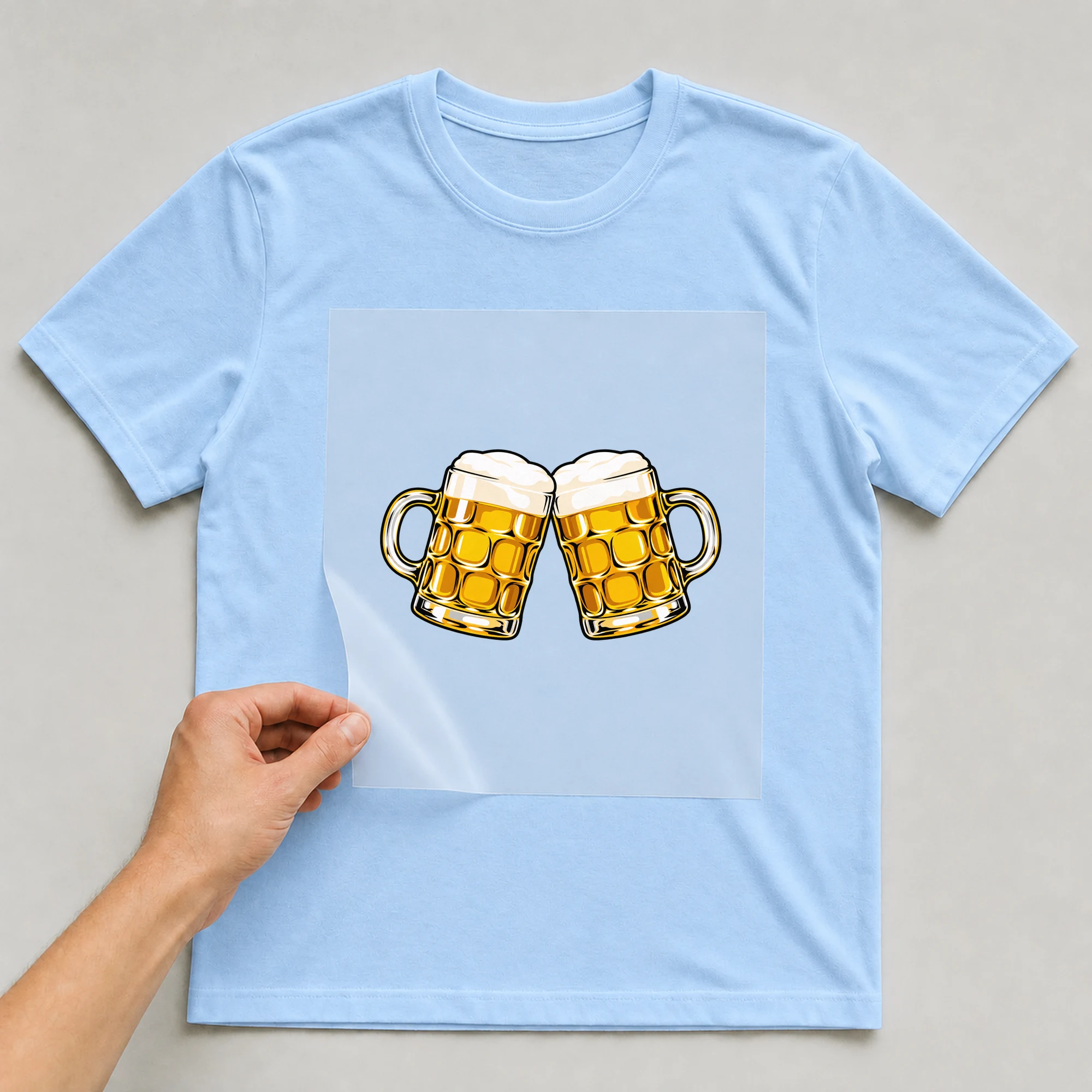 Bügelbild „Maßkrüge Bier“ auf babyblauem T-Shirt, Folie wird aufgelegt