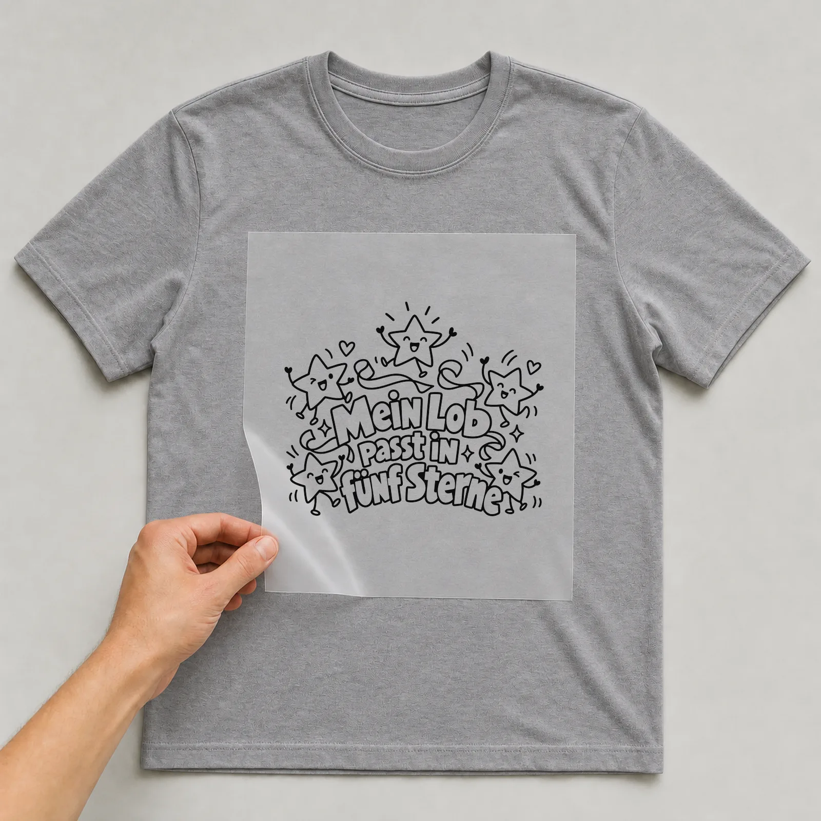 Bügelbild „Mein Lob passt in fünf Sterne“ auf grauem T-Shirt, Folie wird aufgelegt