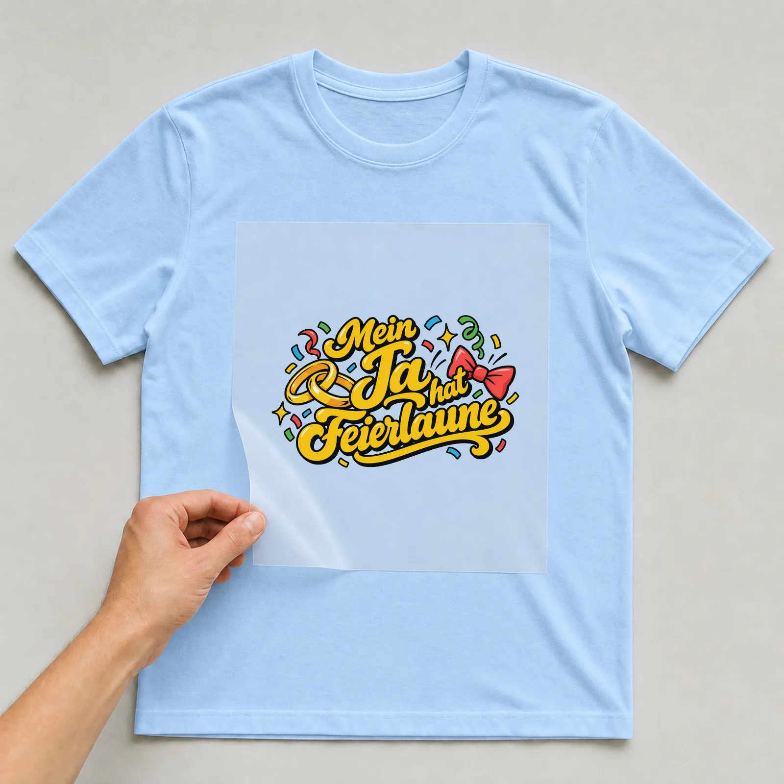 Bügelbild „Mein Ja hat Feierlaune“ auf hellblauem T-Shirt, Folie wird aufgelegt