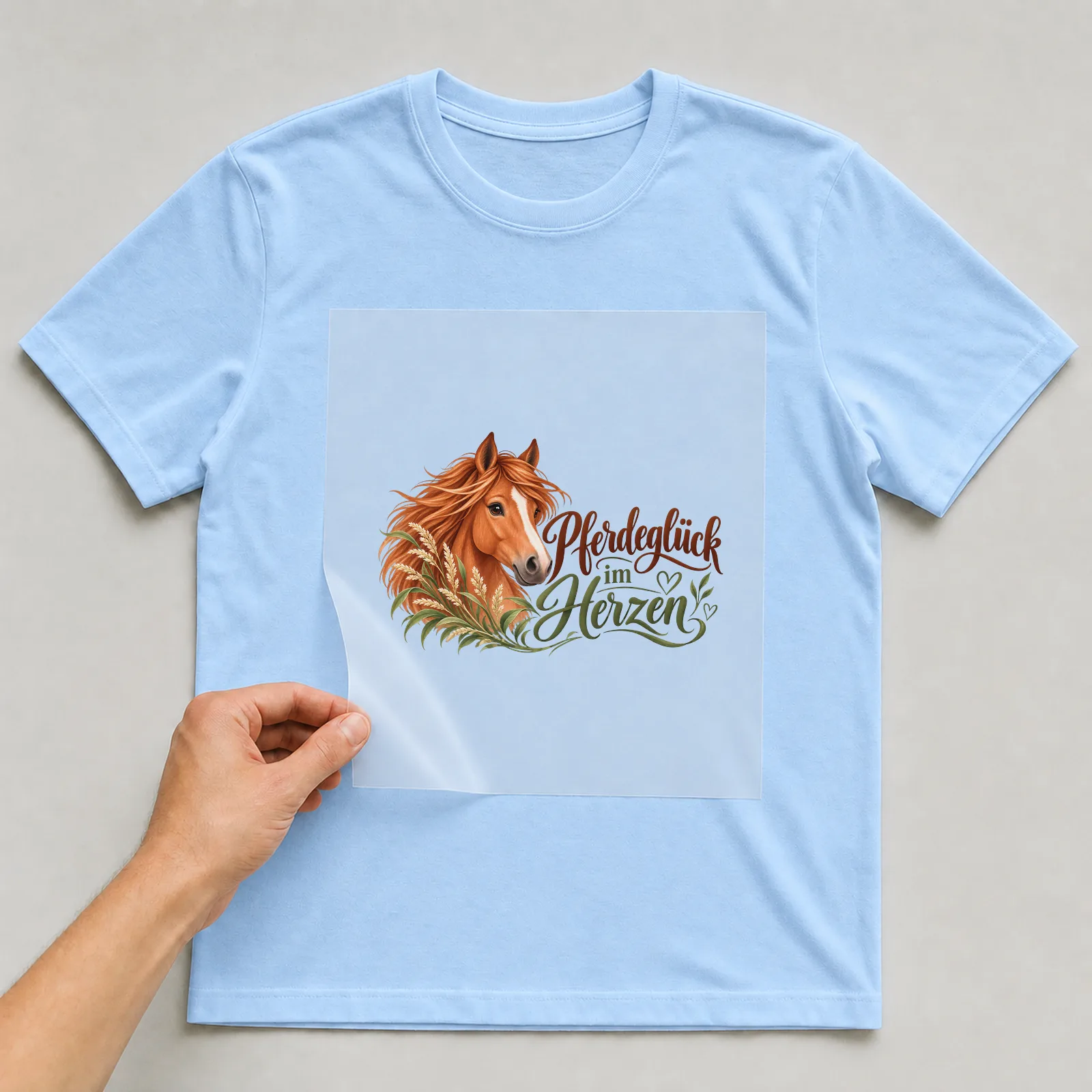 Bügelbild „Pferdeglück im Herzen“ auf hellblauem T-Shirt, Folie wird aufgelegt