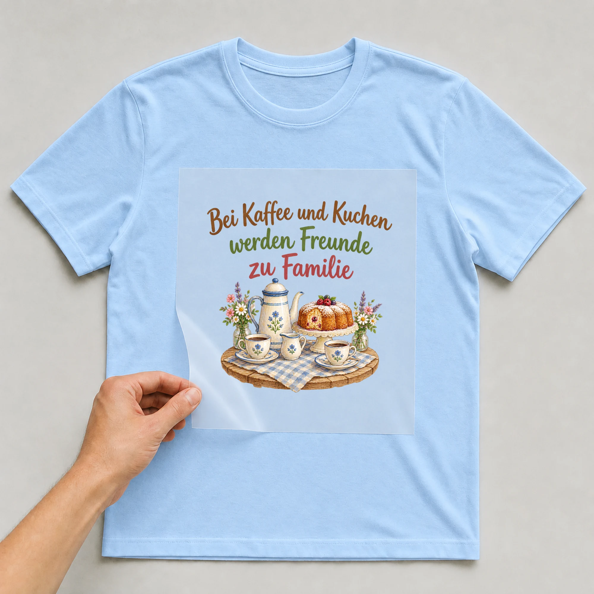 Bügelbild „Bei Kaffee und Kuchen werden Freunde zu Familie“ auf babyblauem T-Shirt, Folie wird aufgelegt