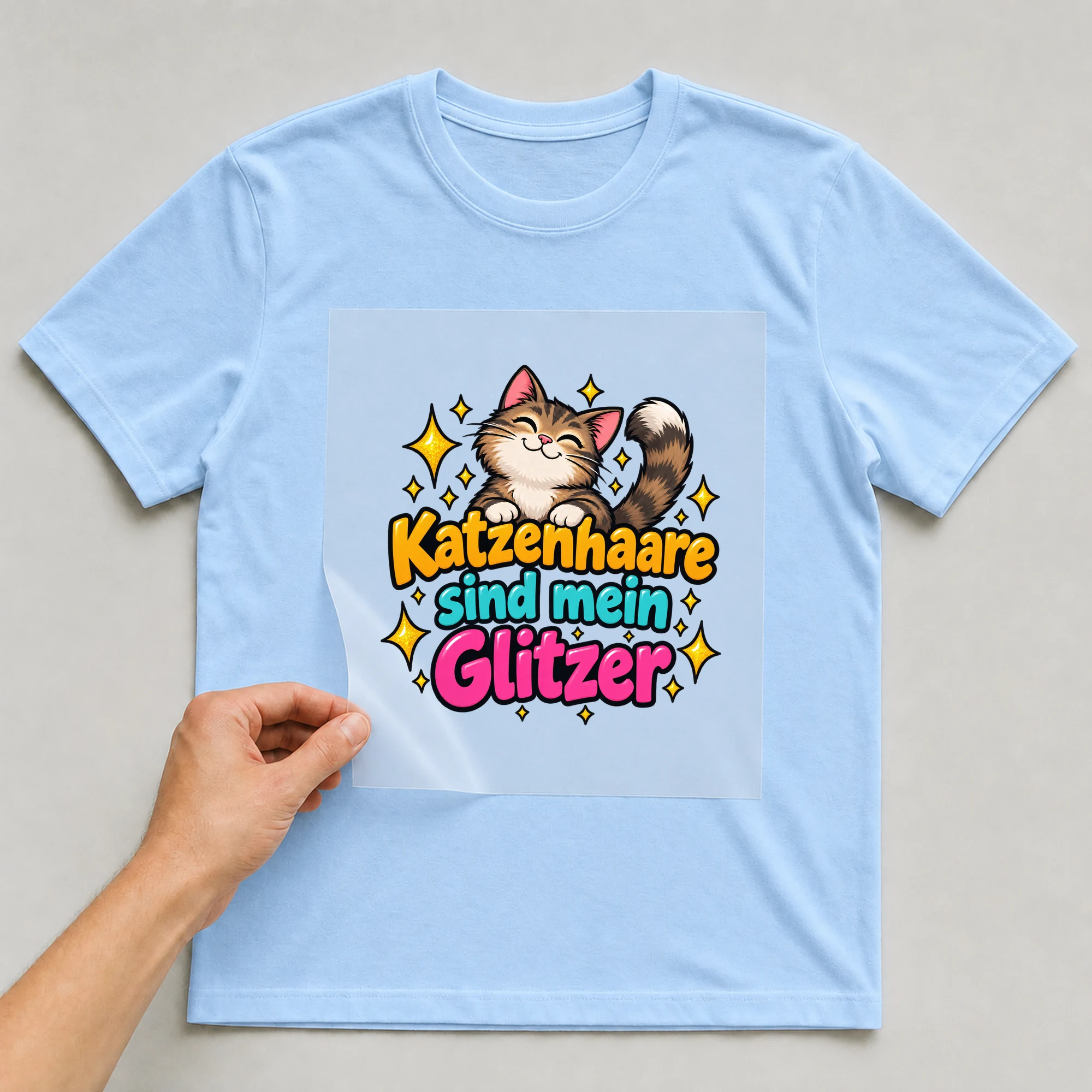 Bügelbild „Katzenhaare sind mein Glitzer“ auf babyblauem T-Shirt, Folie wird aufgelegt