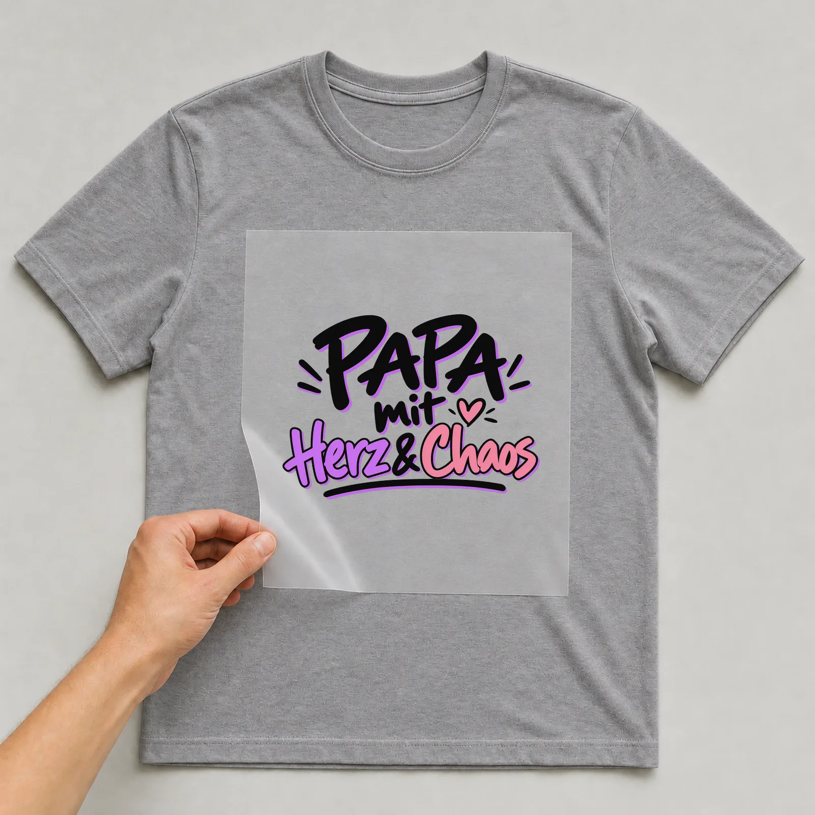 Bügelbild „Papa mit Herz & Chaos“ auf grauem T-Shirt, Folie wird aufgelegt