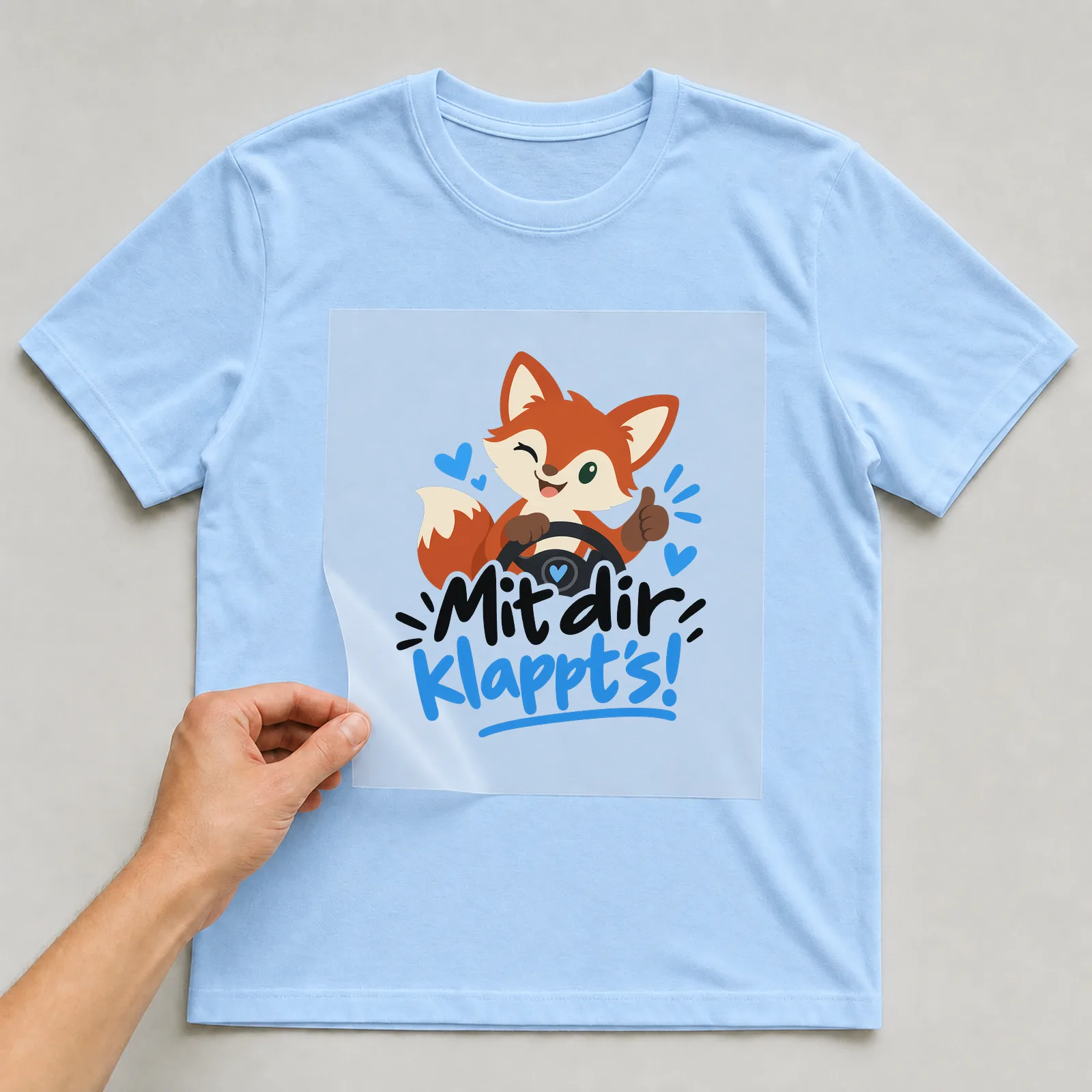Bügelbild „Mit dir klappt’s!“ auf hellblauem T-Shirt, Folie wird aufgelegt