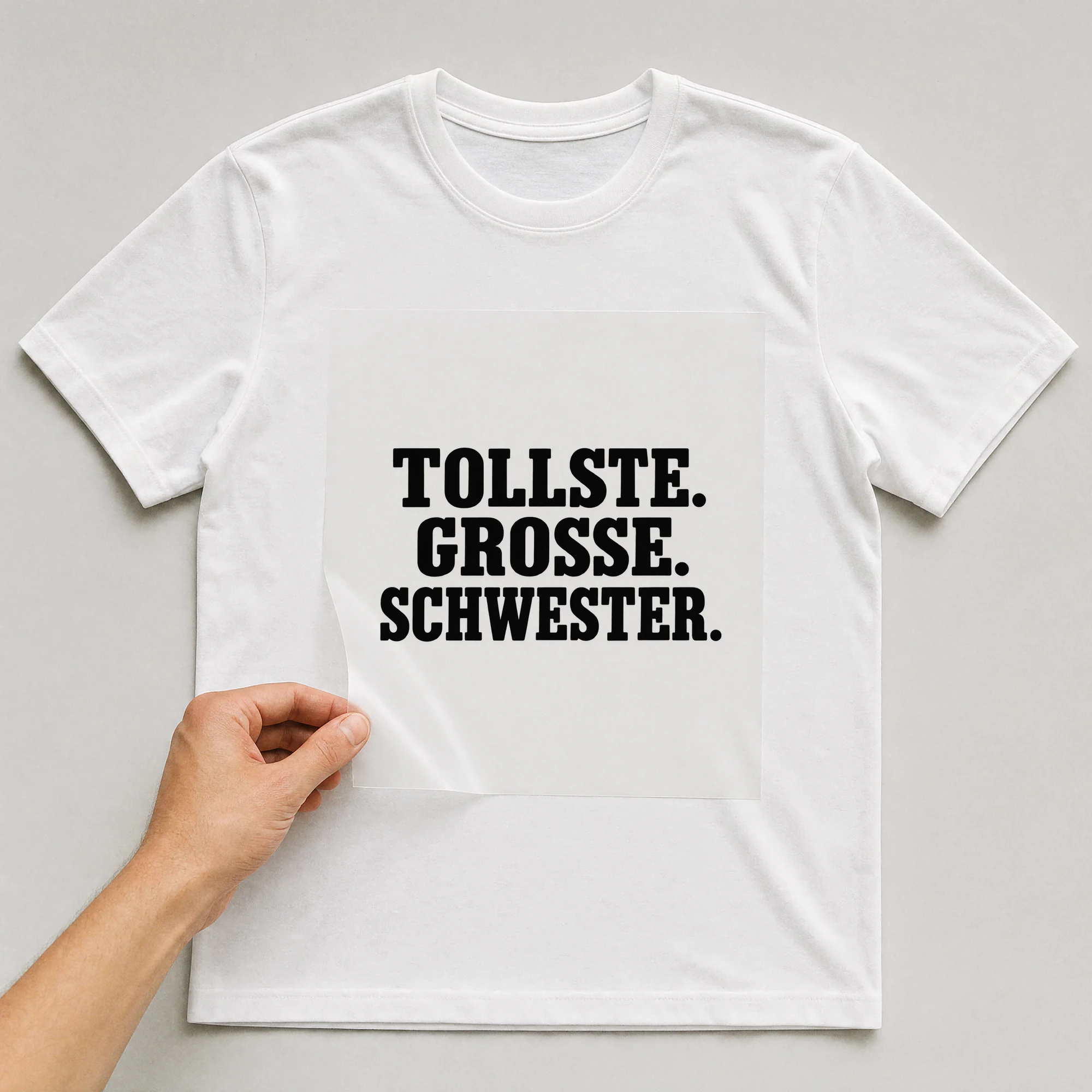 Bügelbild „Tollste. Grosse. Schwester.“ auf weißem T-Shirt, Folie wird aufgelegt