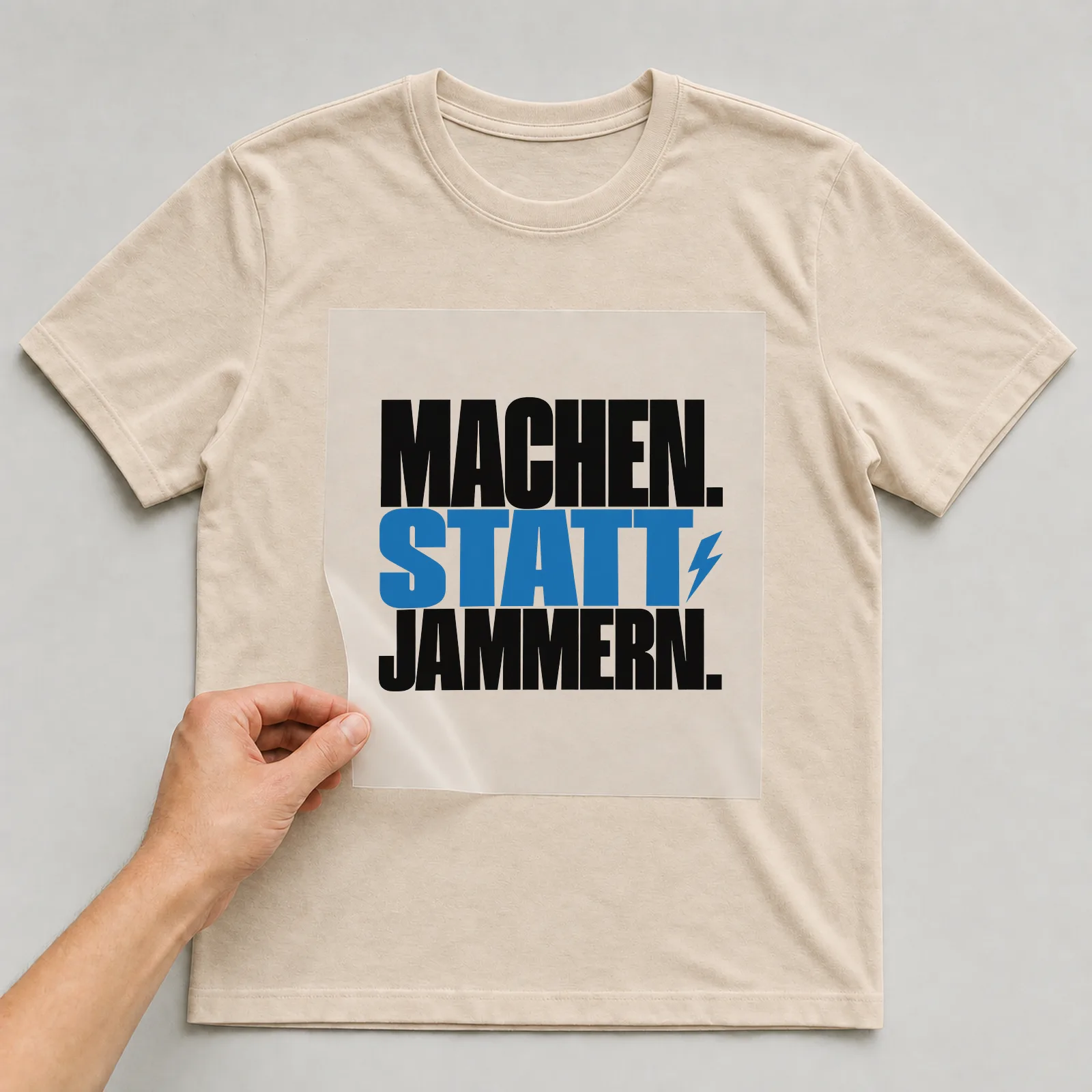Bügelbild „Machen. Statt jammern.“ auf beigem T-Shirt, Folie wird aufgelegt