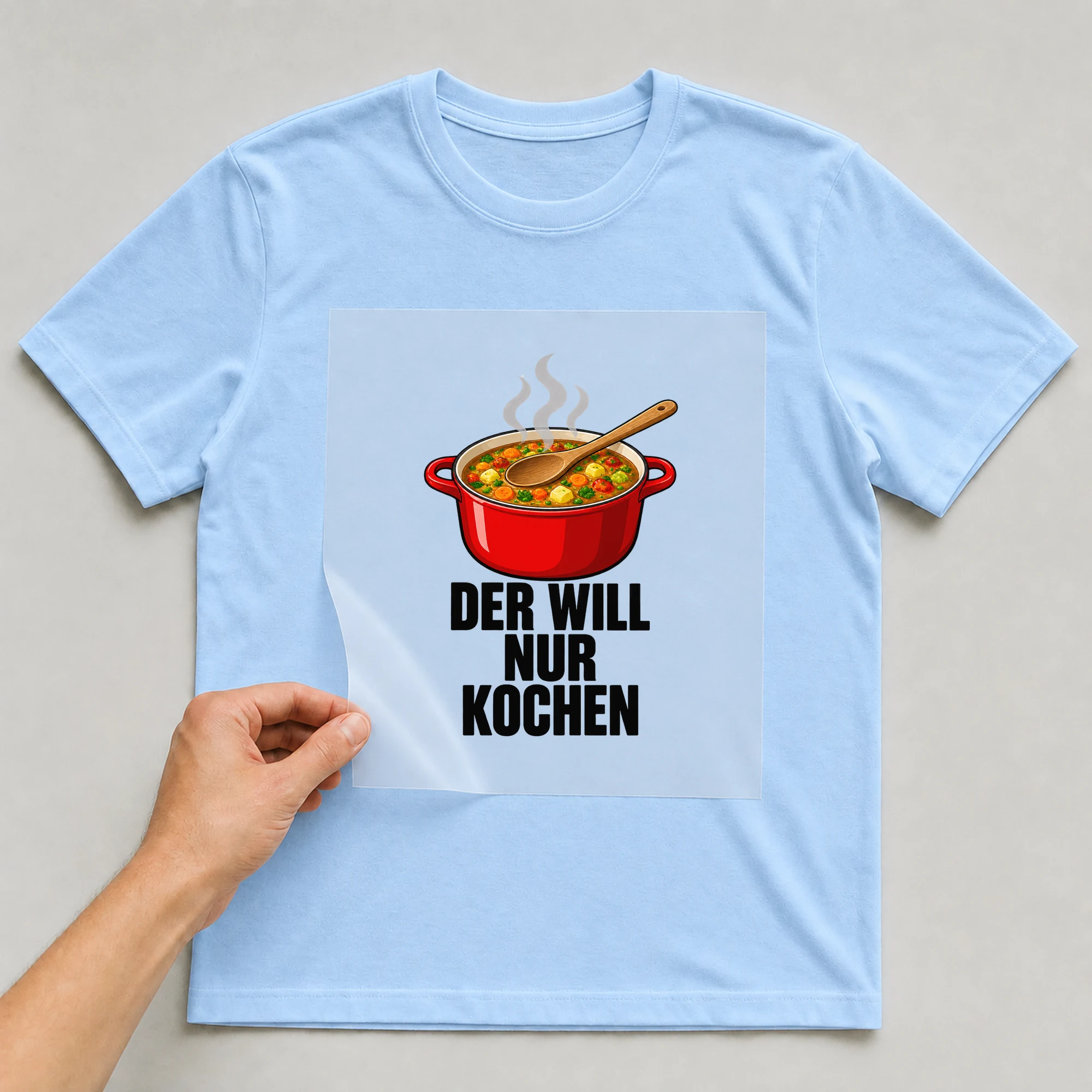 Bügelbild „Der will nur kochen“ auf babyblauem T-Shirt, Folie wird aufgelegt