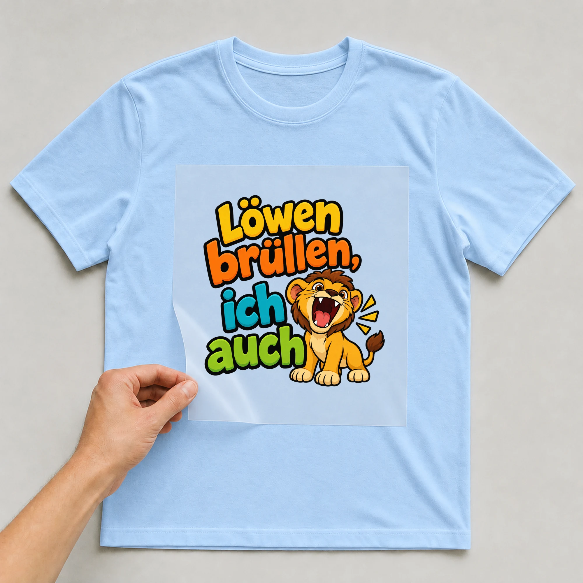 Bügelbild „Löwen brüllen, ich auch“ auf babyblauem T-Shirt, Folie wird aufgelegt