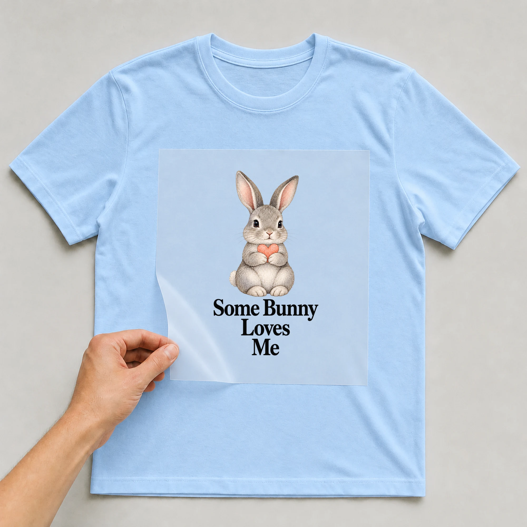 Bügelbild „Some Bunny Loves Me“ auf babyblauem T-Shirt, Folie wird aufgelegt