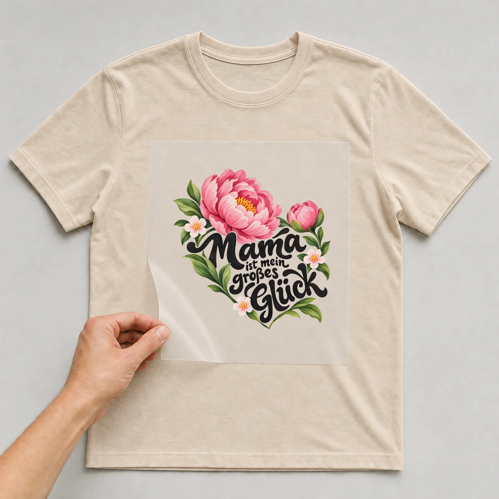 Bügelbild „Mama ist mein großes Glück“ auf beigem T-Shirt, Folie wird aufgelegt
