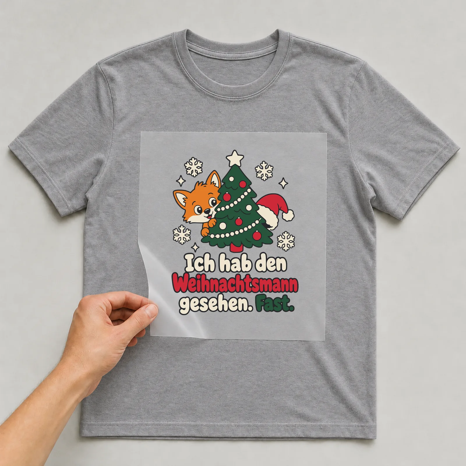 Bügelbild Ich hab den Weihnachtsmann gesehen. Fast. auf grauem T-Shirt, Folie wird aufgelegt