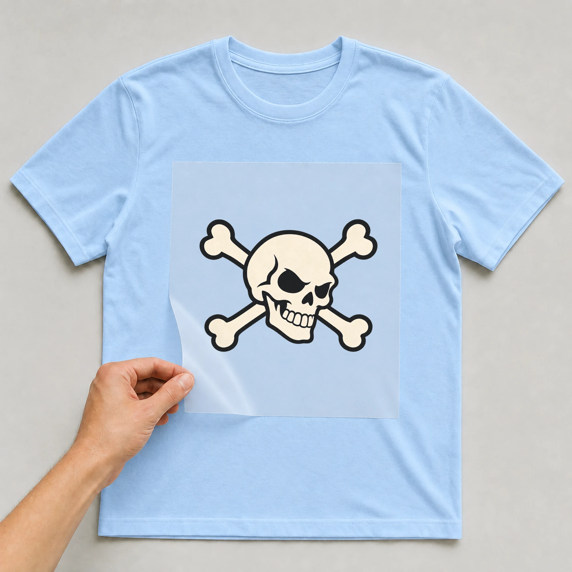 Bügelbild „Totenkopf Und Knochen“ auf babyblauem T-Shirt, Folie wird aufgelegt