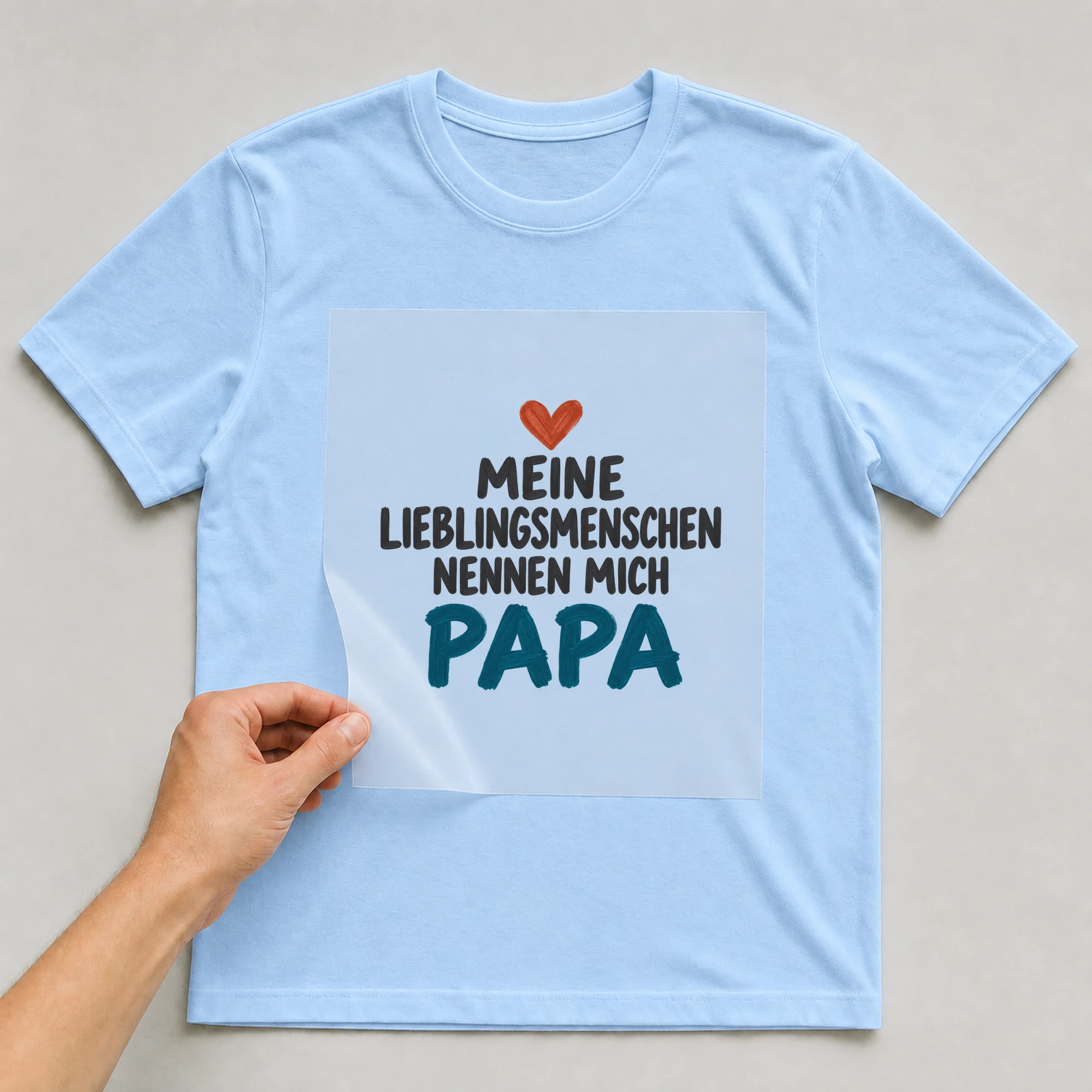 Bügelbild „Meine Lieblingsmenschen Nennen mich Papa“ auf babyblauem T-Shirt, Folie wird aufgelegt