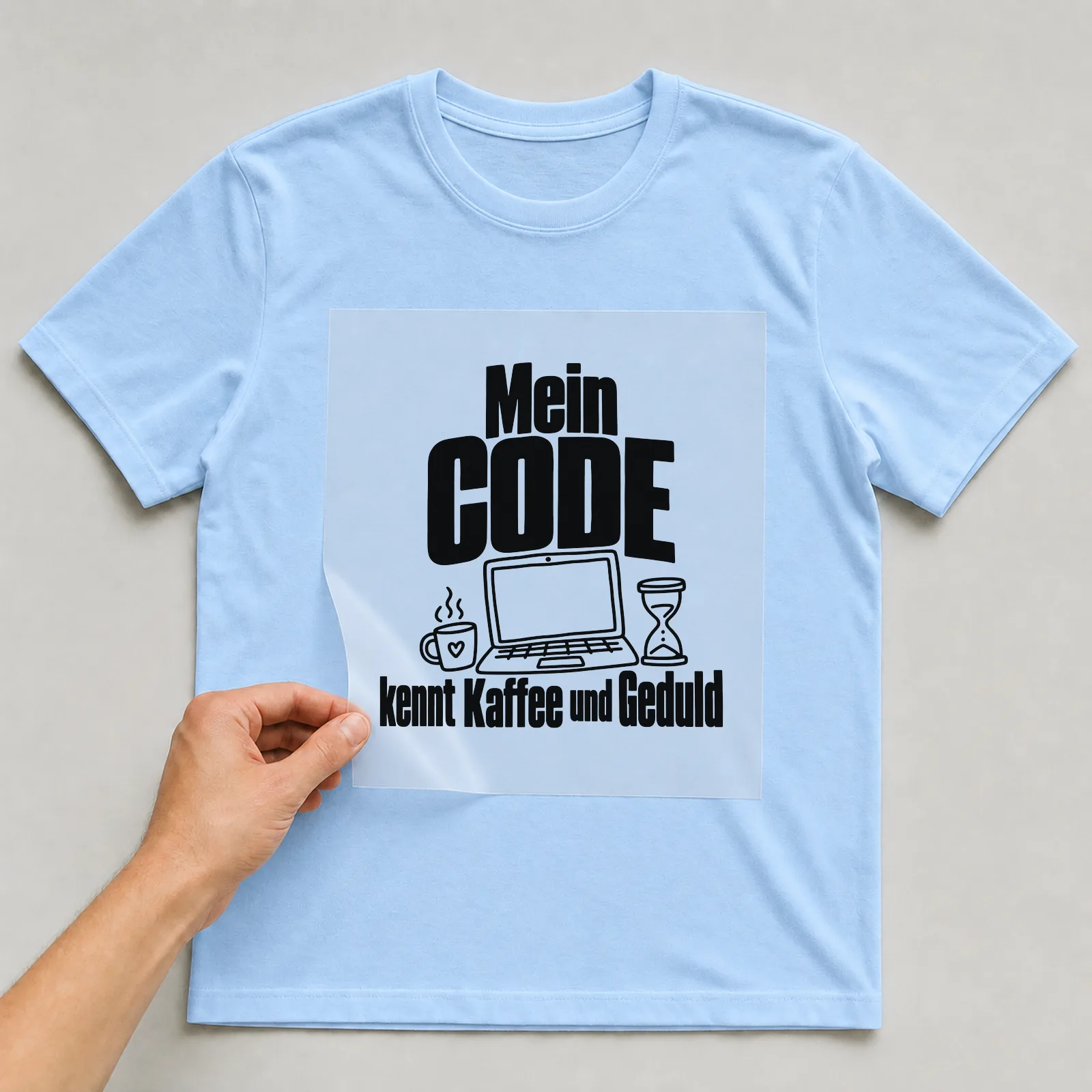 Bügelbild „Mein Code kennt Kaffee und Geduld“ auf hellblauem T-Shirt, Folie wird aufgelegt