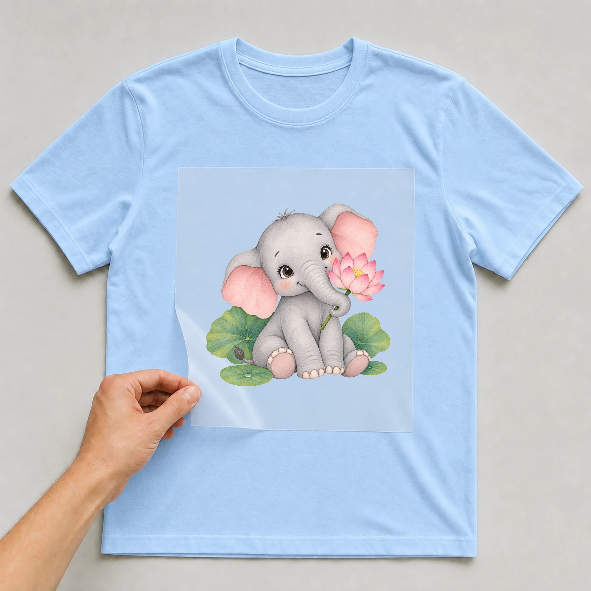 Bügelbild „Elefant mit lotusblueten motiv ohne text“ auf babyblauem T-Shirt, Folie wird aufgelegt