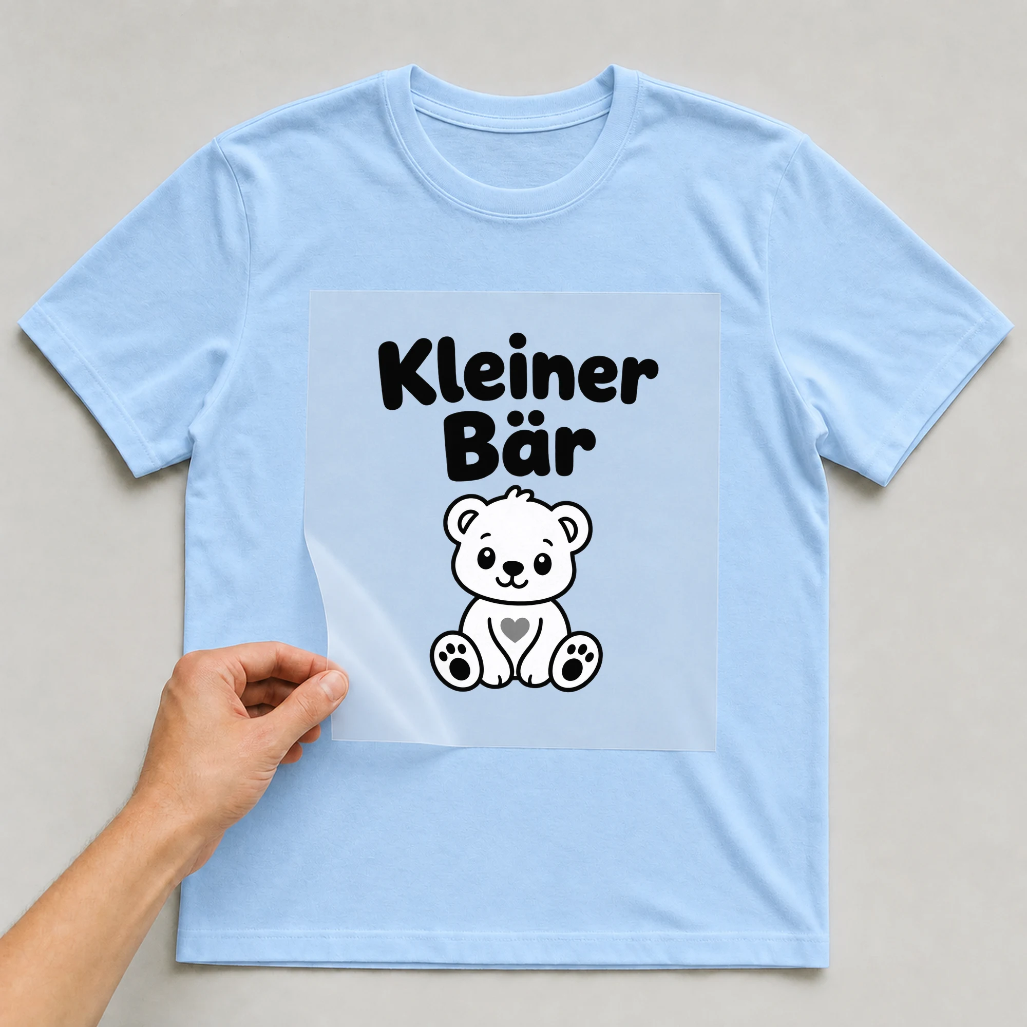 Bügelbild „Kleiner Bär“ auf babyblauem T-Shirt, Folie wird aufgelegt