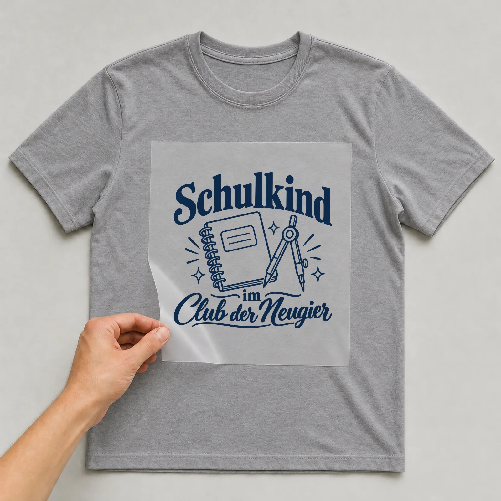 Bügelbild „Schulkind im Club der Neugier“ auf grauem T-Shirt, Folie wird aufgelegt