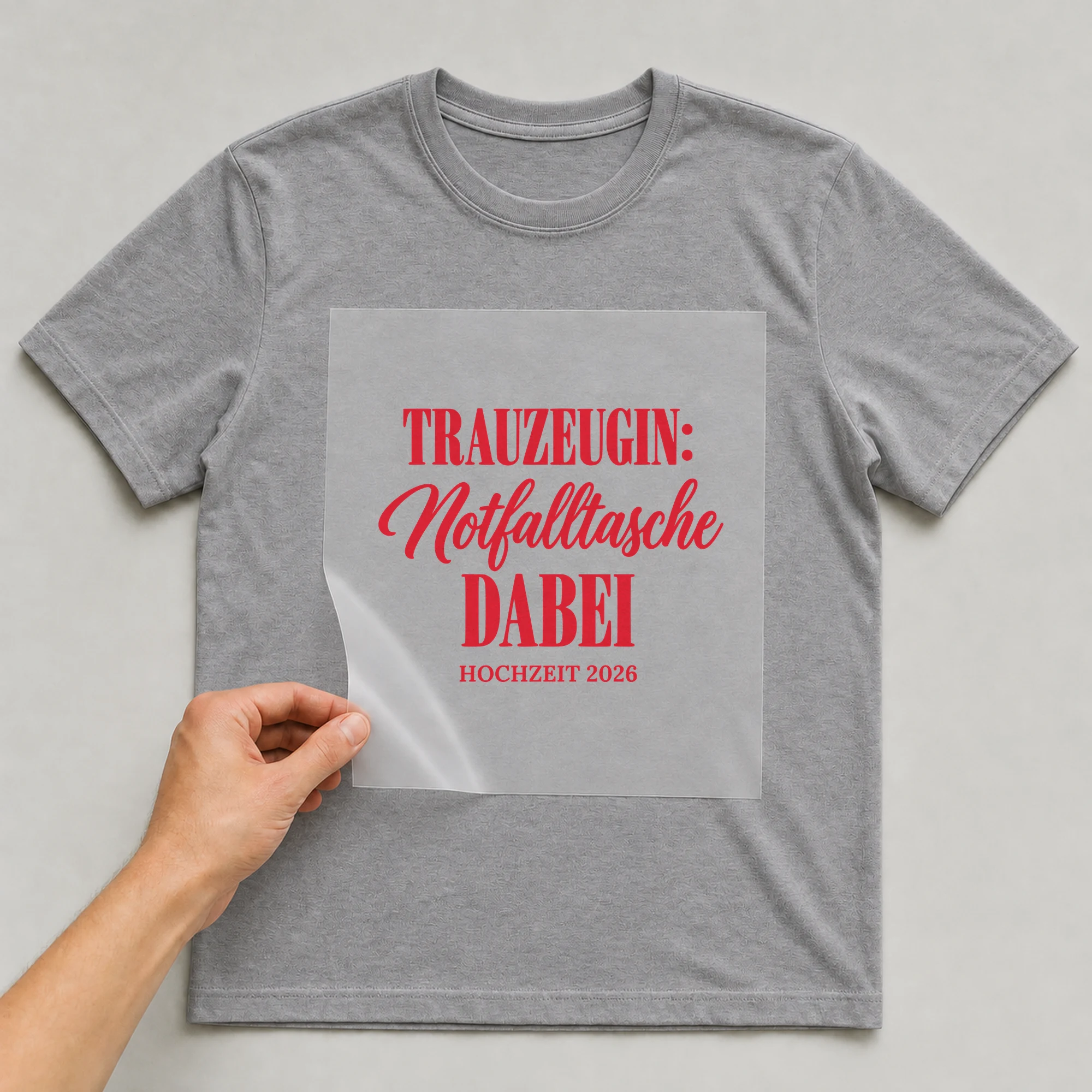 Bügelbild Trauzeugin: Notfalltasche dabei mit Jahr auf grauem T-Shirt, Folie wird aufgelegt