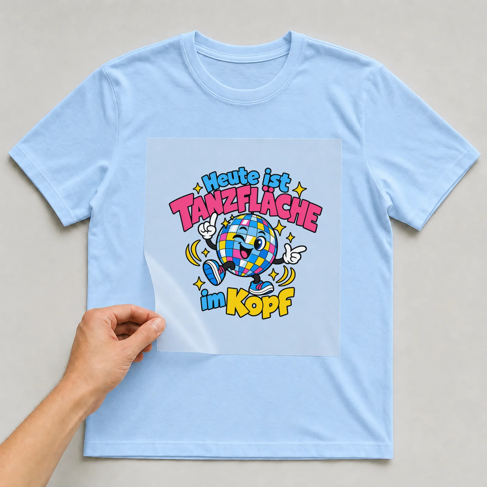 Bügelbild „Heute ist Tanzfläche im Kopf“ auf hellblauem T-Shirt, Folie wird aufgelegt