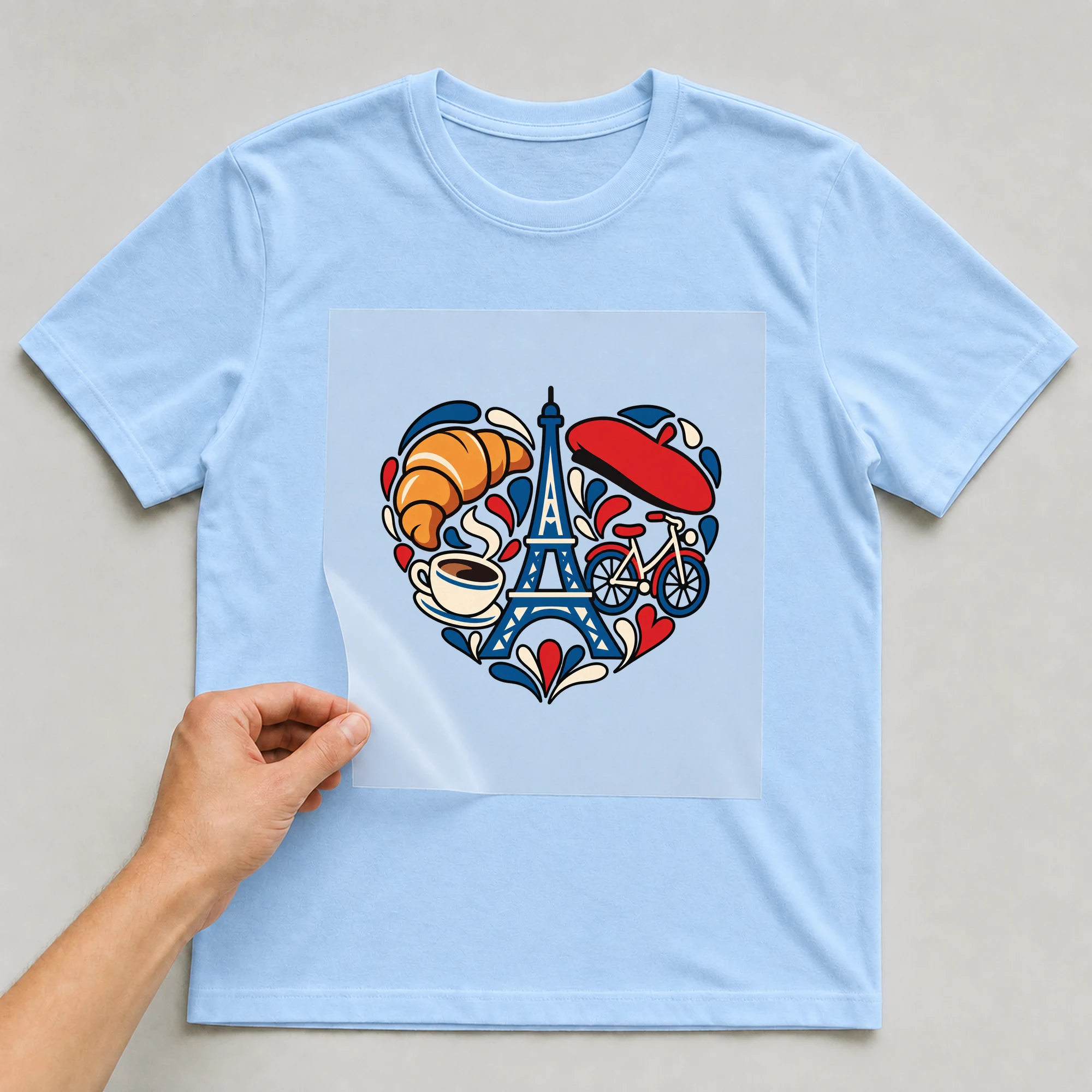 Bügelbild „Paris Love Heart“ auf babyblauem T-Shirt, Folie wird aufgelegt