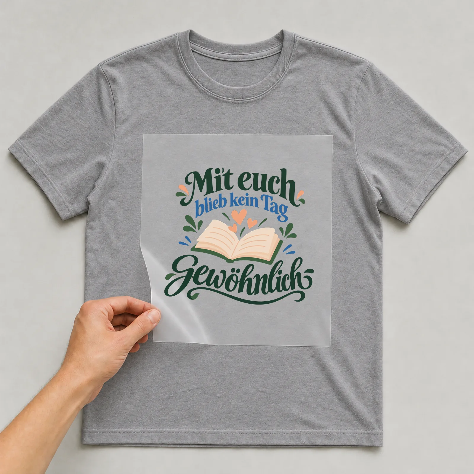 Bügelbild „Mit euch blieb kein Tag gewöhnlich“ auf grauem T-Shirt, Folie wird aufgelegt