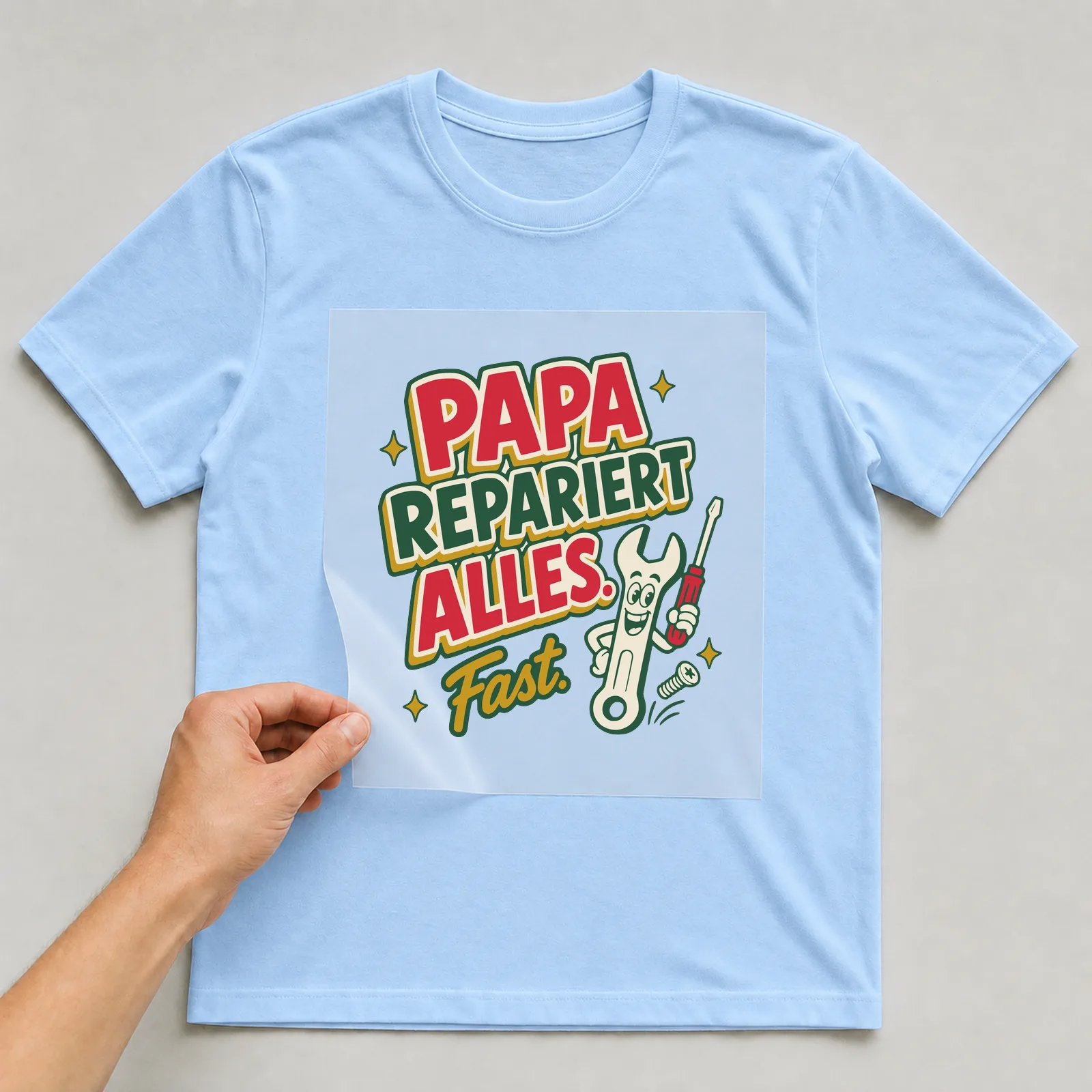 Bügelbild Papa repariert alles. Fast. auf hellblauem T-Shirt, Folie wird aufgelegt