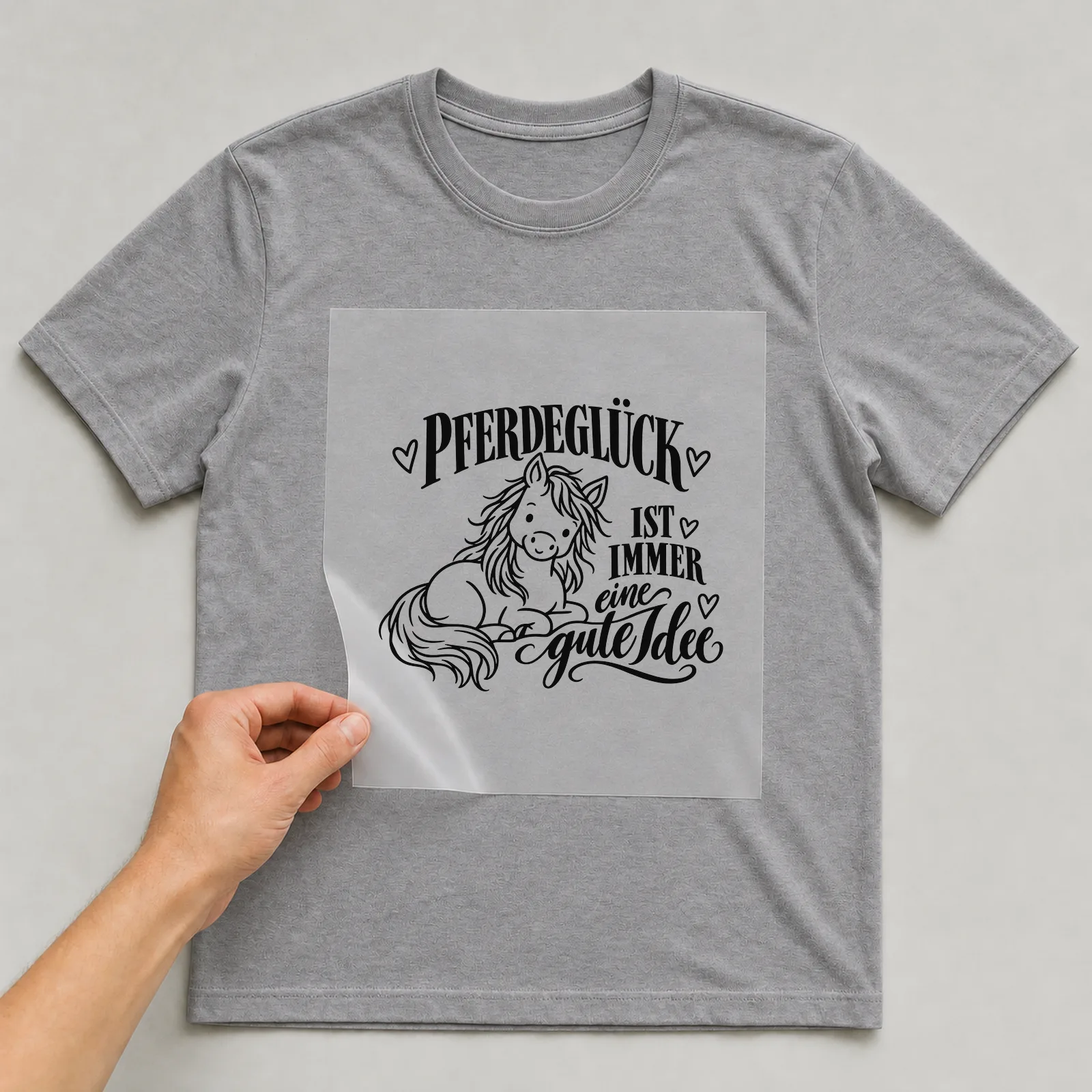 Bügelbild „Pferdeglück ist immer eine gute Idee“ auf grauem T-Shirt, Folie wird aufgelegt