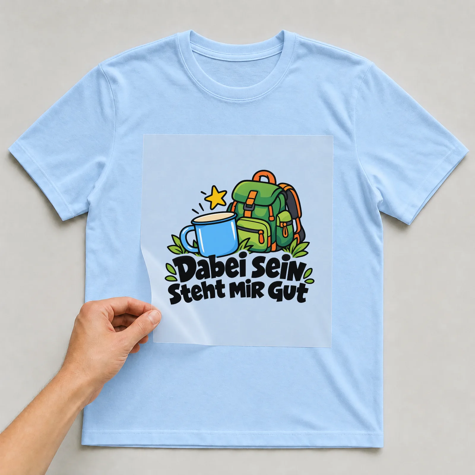 Bügelbild „Dabei sein steht MIR GUT“ auf hellblauem T-Shirt, Folie wird aufgelegt