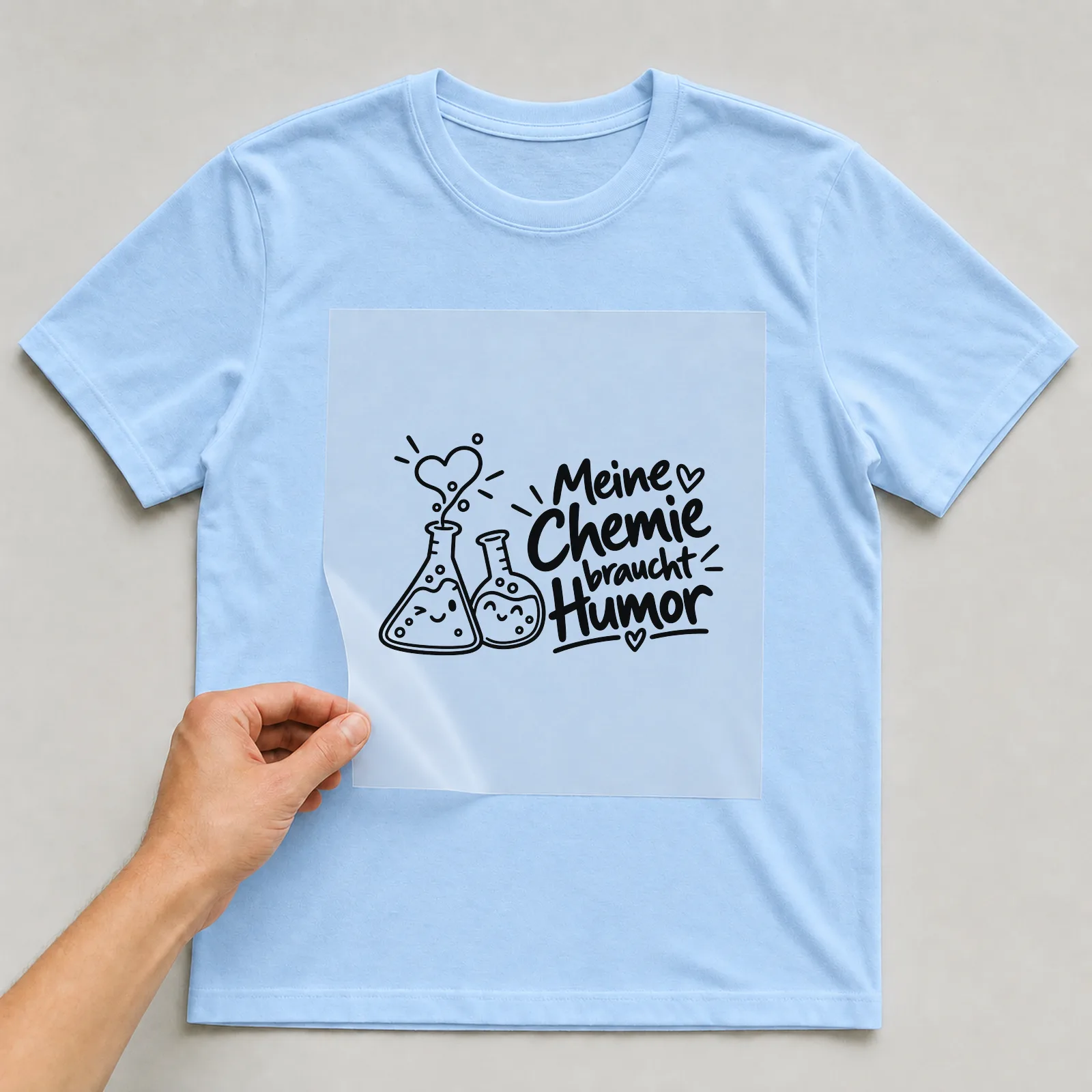 Bügelbild „Meine Chemie braucht Humor“ auf hellblauem T-Shirt, Folie wird aufgelegt