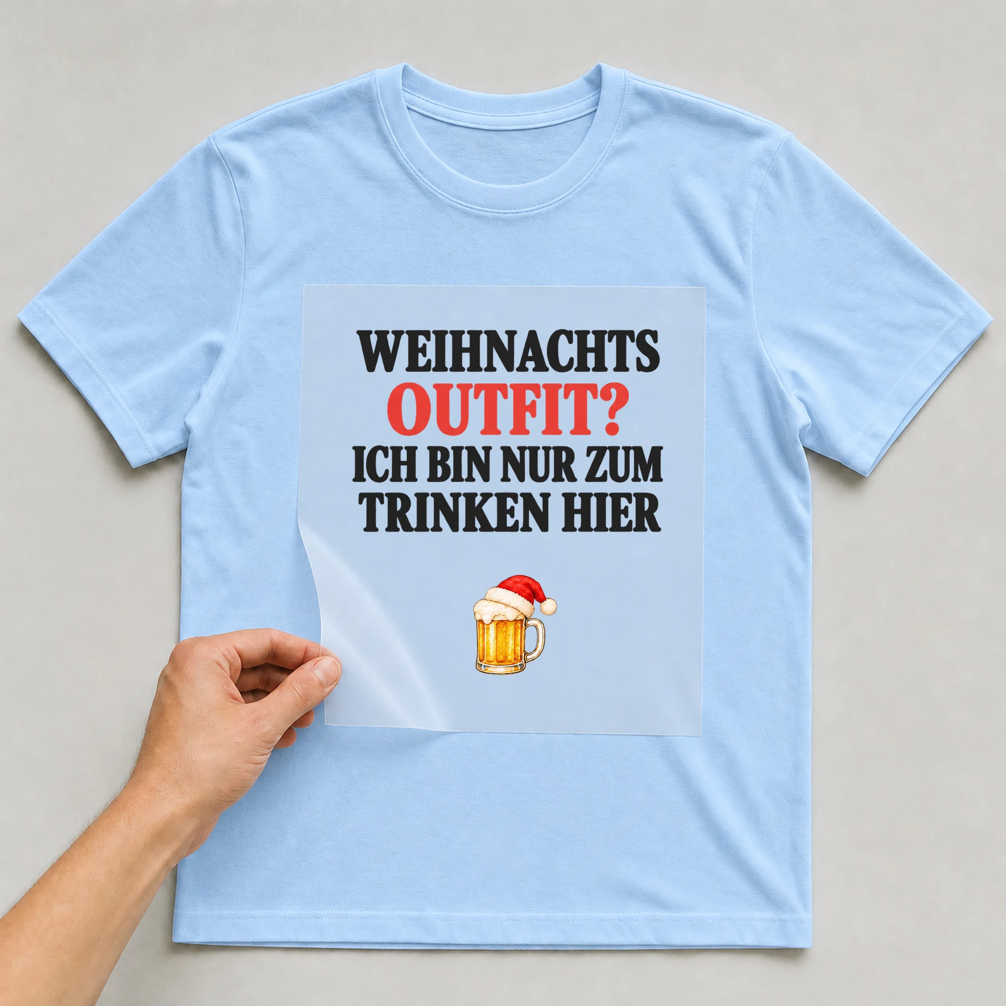 Bügelbild „WEIHNACHTS OUTFIT? ICH BIN NUR ZUM TRINKEN HIER“ auf babyblauem T-Shirt, Folie wird aufgelegt