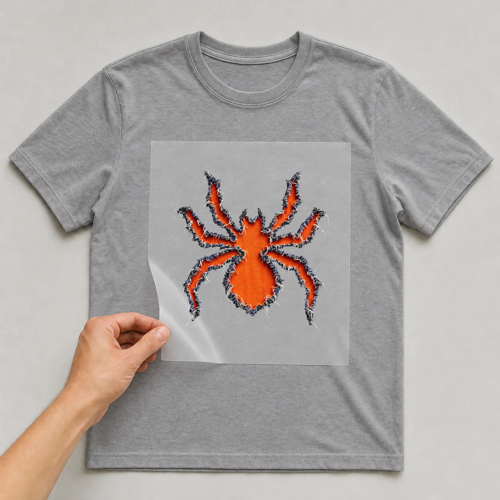 Bügelbild Spinne Zerrissen (Halloween) auf grauem T-Shirt, Folie wird aufgelegt