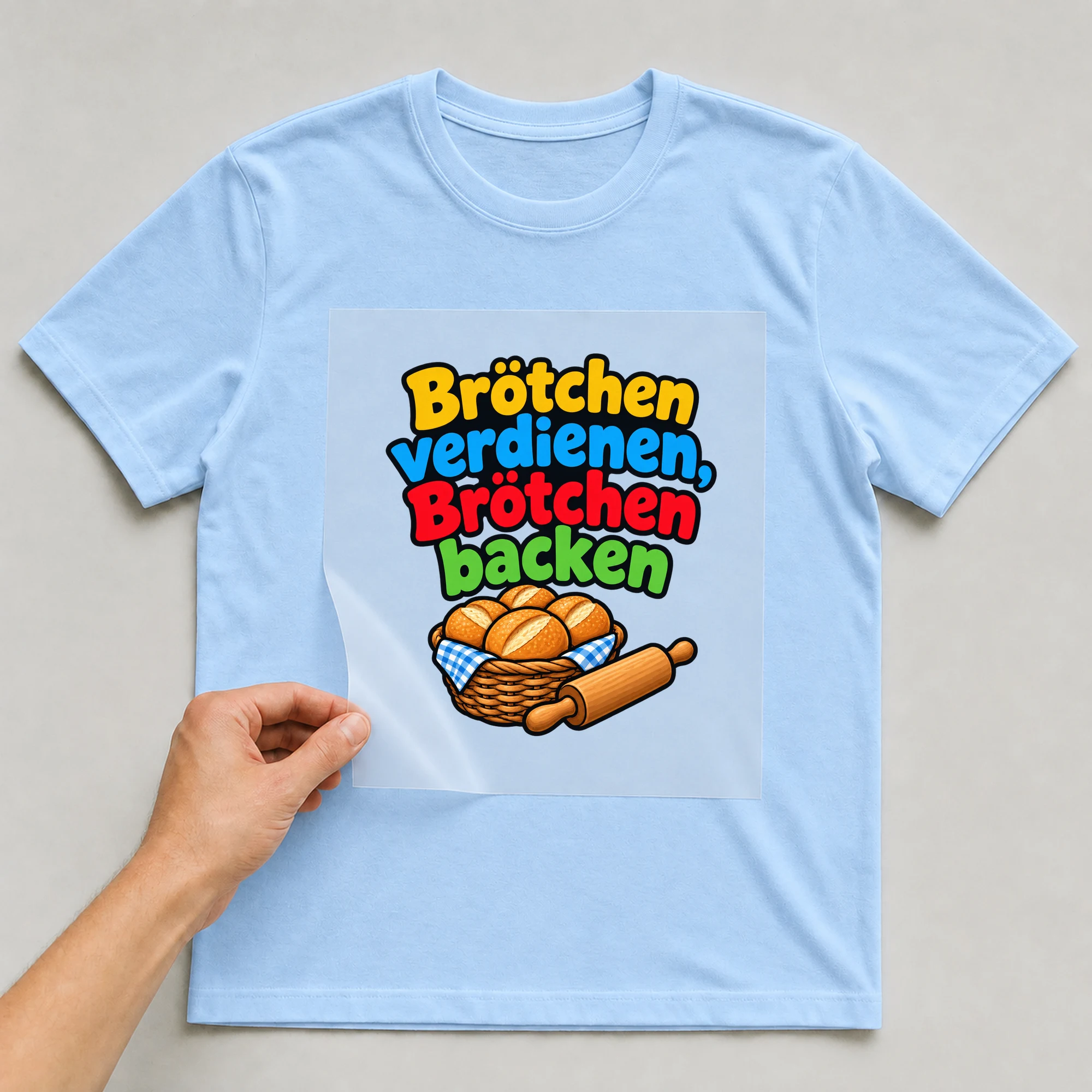 Bügelbild „Brötchen verdienen, Brötchen backen“ auf babyblauem T-Shirt, Folie wird aufgelegt