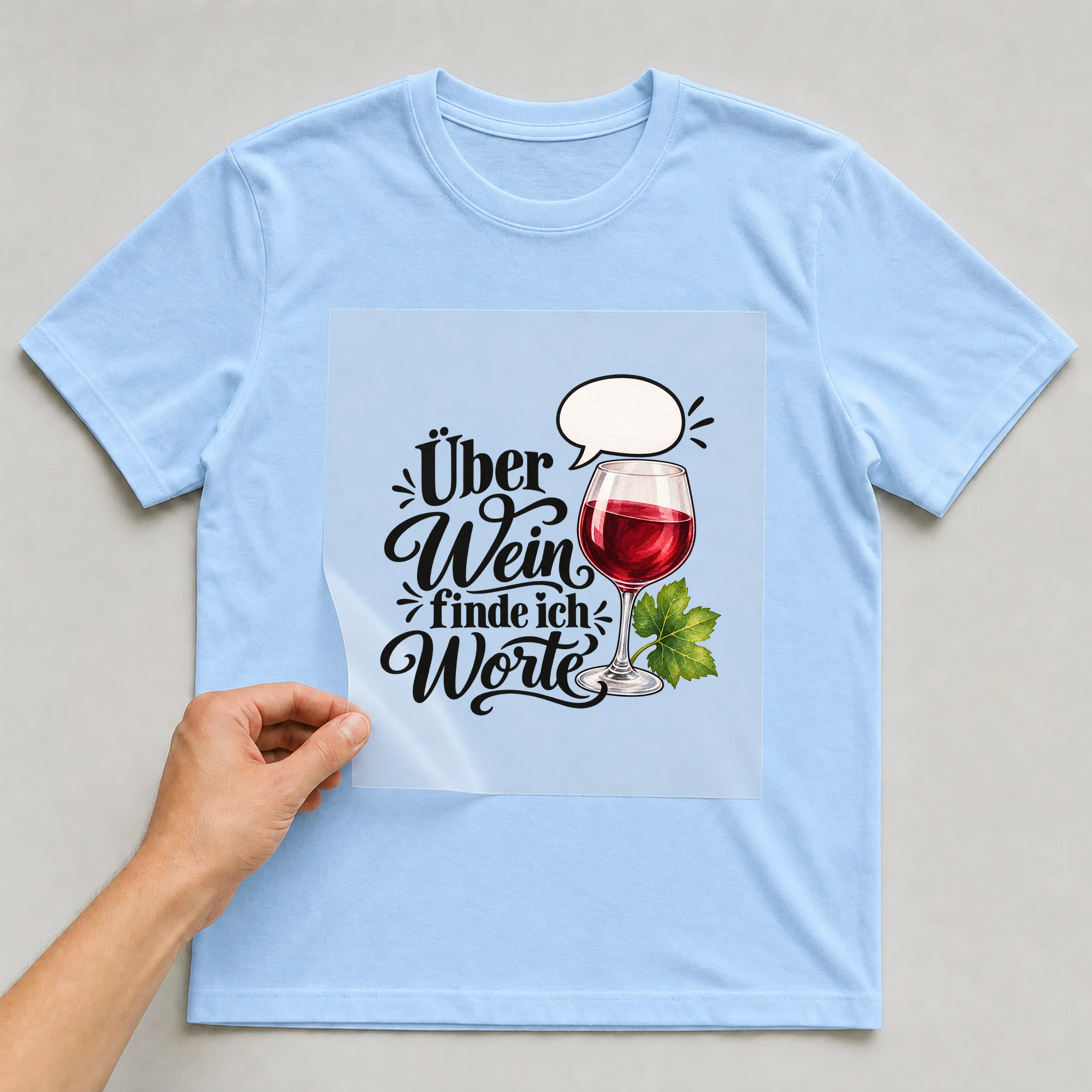 Bügelbild „Über Wein finde ich Worte“ auf babyblauem T-Shirt, Folie wird aufgelegt