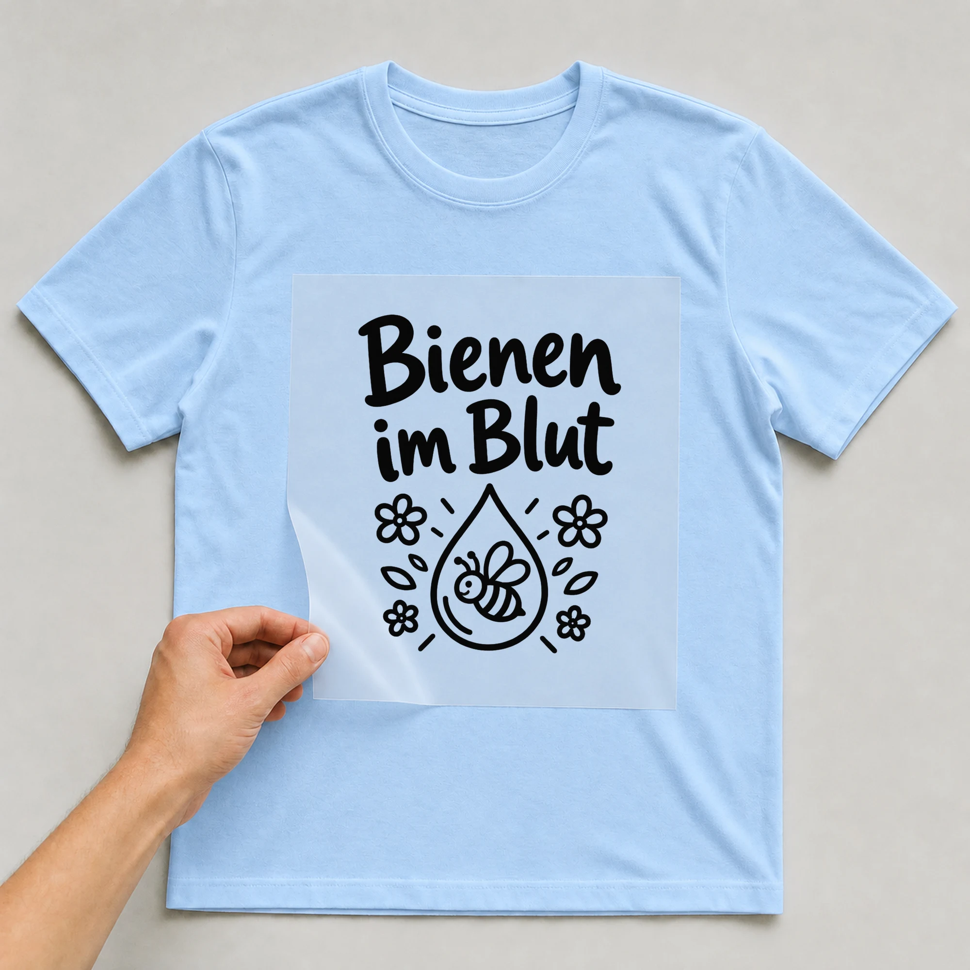 Bügelbild „Bienen im Blut“ auf babyblauem T-Shirt, Folie wird aufgelegt