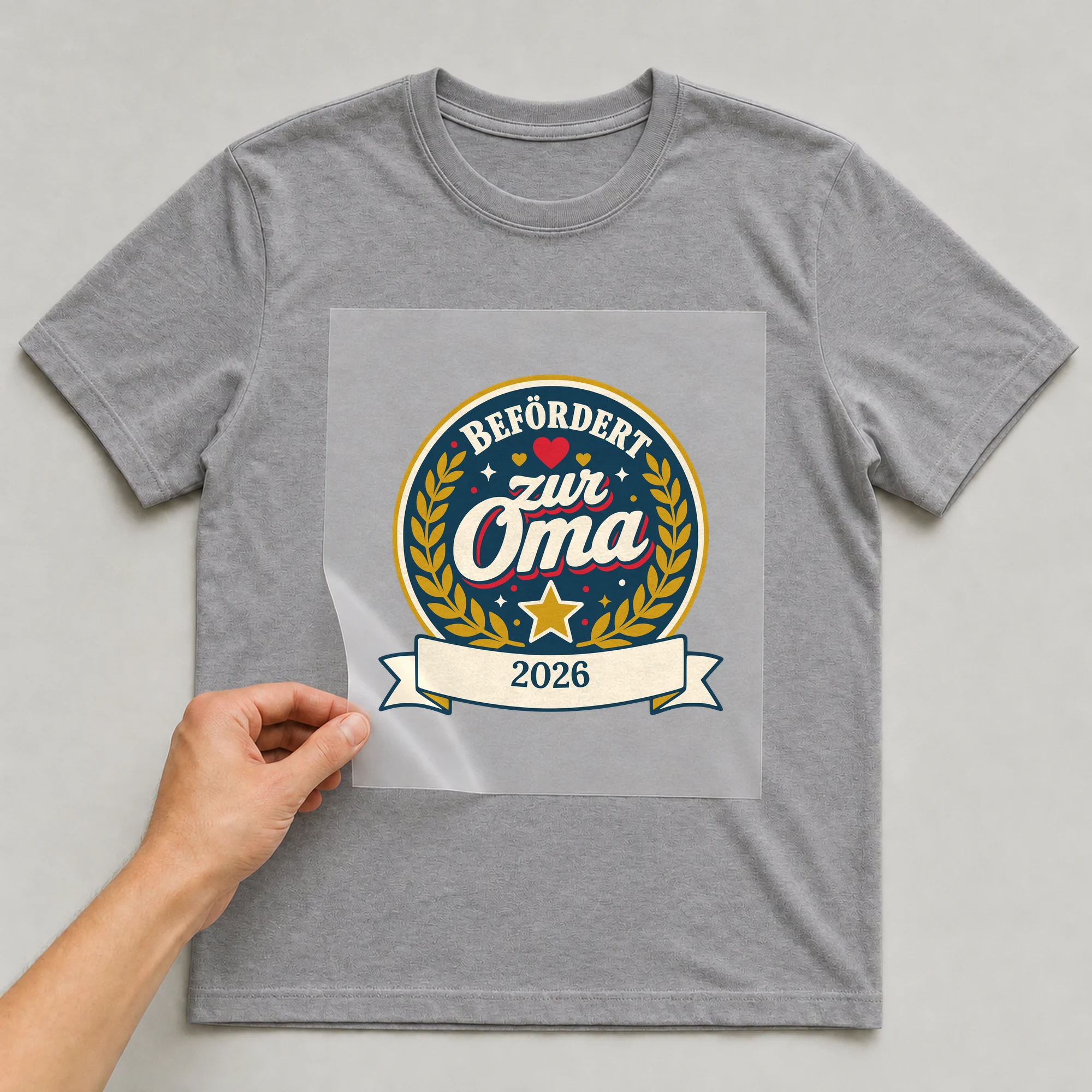 Bügelbild Befördert zur Oma mit Jahr auf grauem T-Shirt, Folie wird aufgelegt