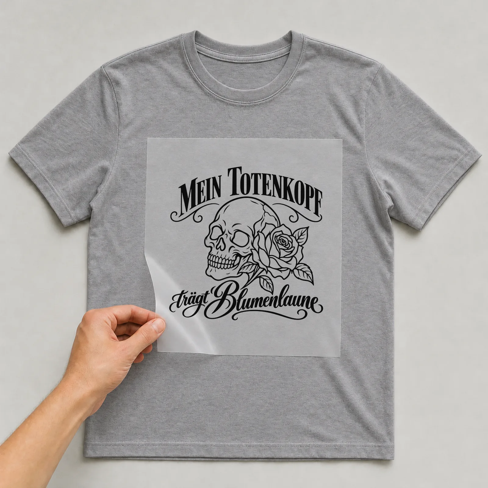 Bügelbild „Mein Totenkopf trägt Blumenlaune“ auf grauem T-Shirt, Folie wird aufgelegt