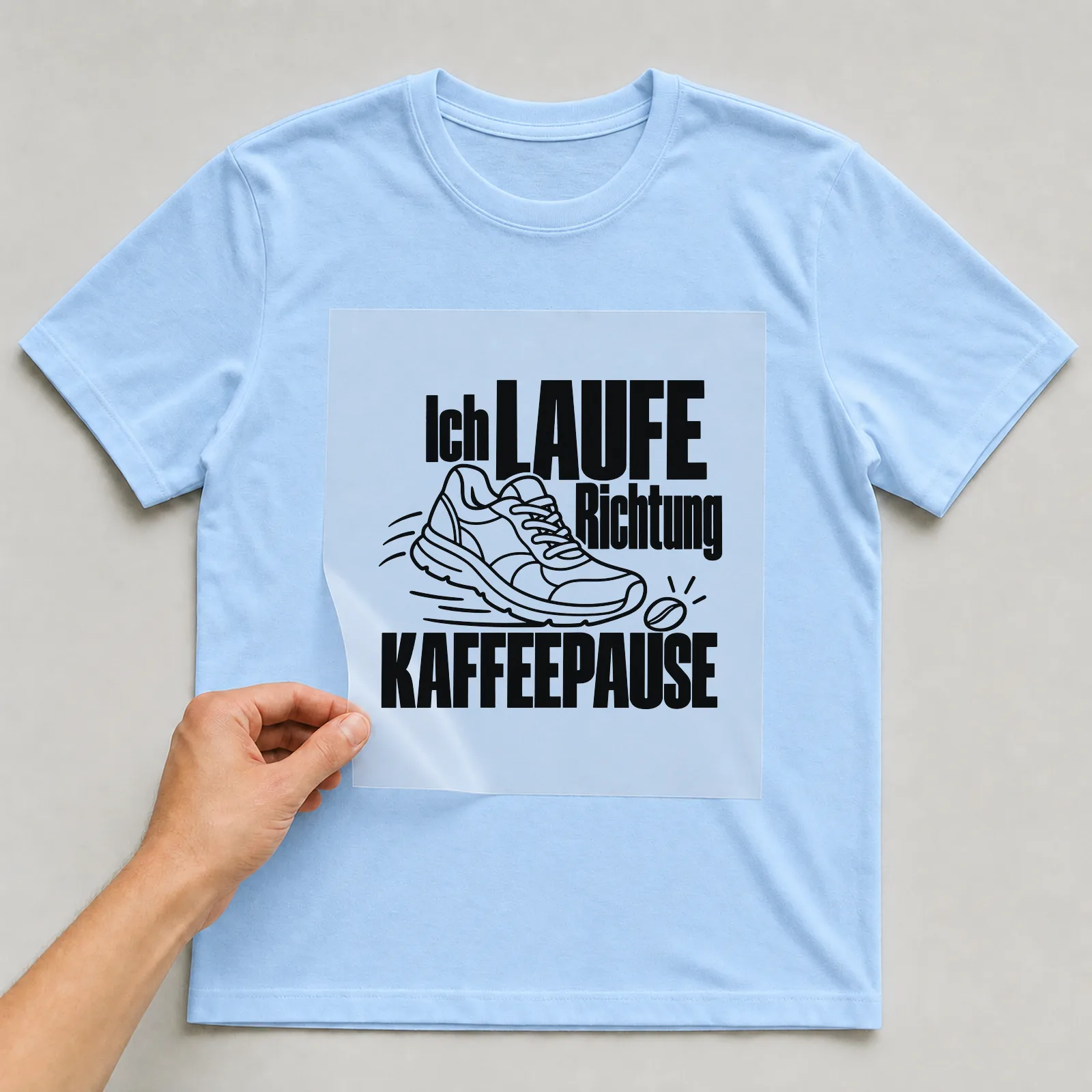 Bügelbild „Ich laufe Richtung Kaffeepause“ auf hellblauem T-Shirt, Folie wird aufgelegt